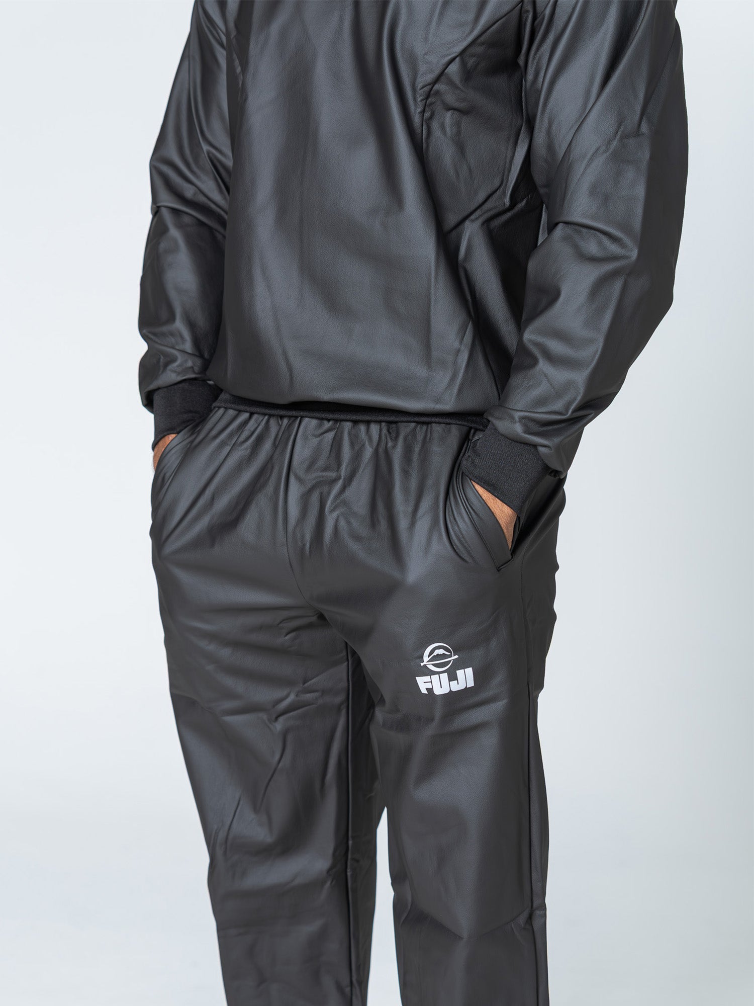 A person is wearing the Grappling Sauna Suit Black, standing with hands in pockets. The image shows only the body from shoulders down against a plain white background.