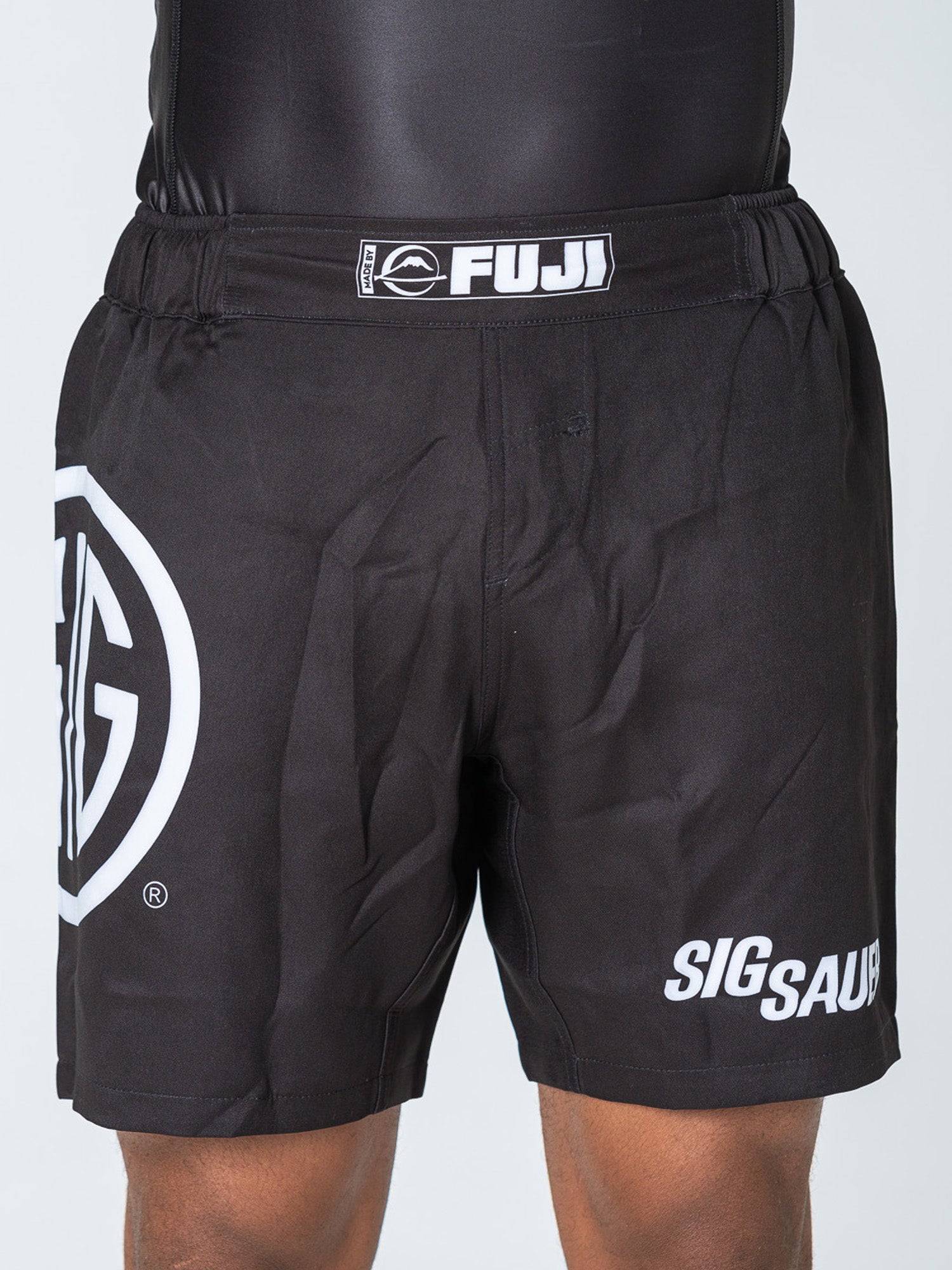 Person wearing Sig Sauer Lightweight Shorts Black, featuring white logos and lettering on the left leg and waistband. The image highlights the shorts from waist to mid-thigh.