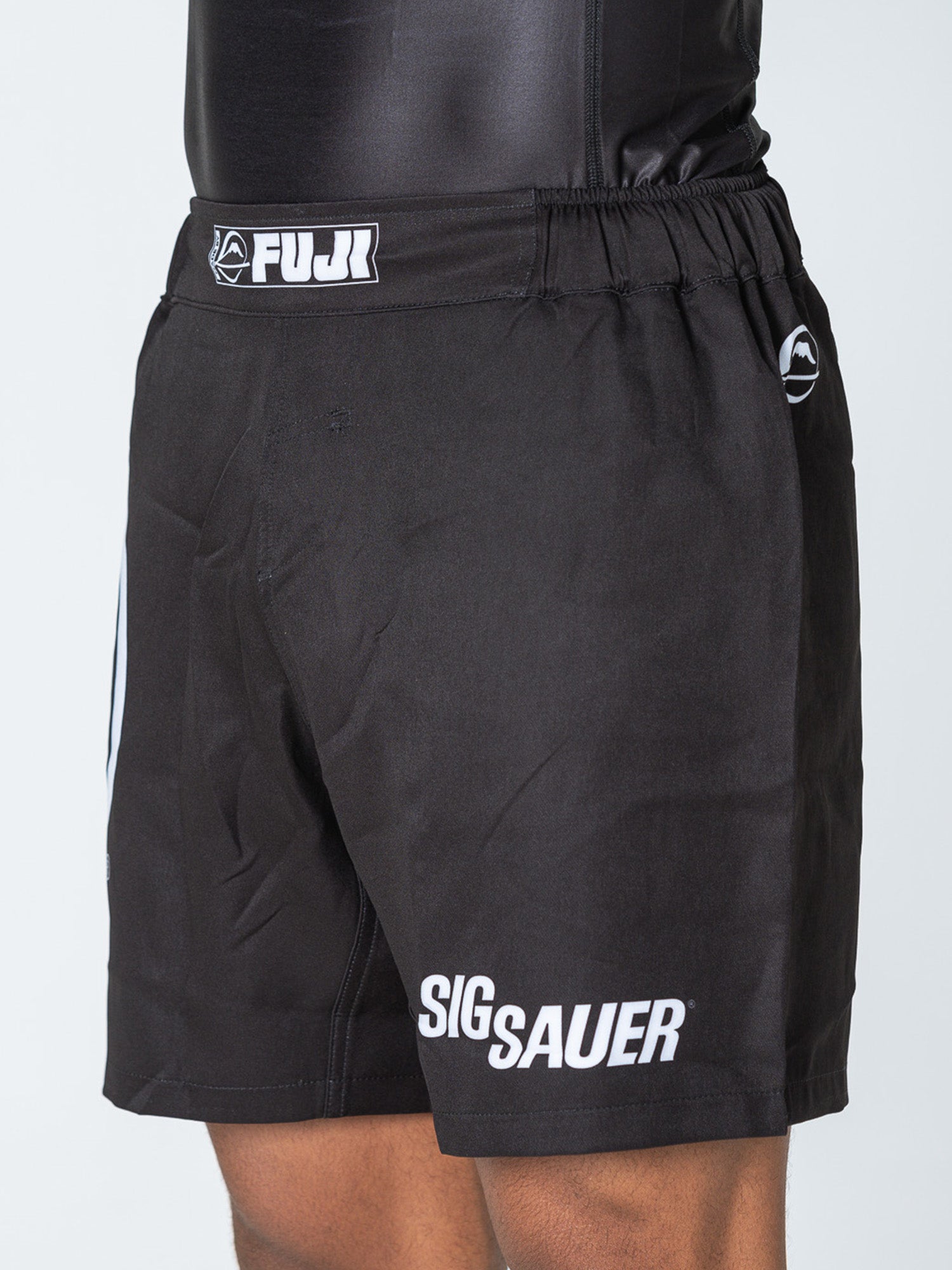 A person wears Sig Sauer Lightweight Shorts Black with FUJI on the waistband, SIG SAUER on the left leg, a fitted waistband, simple design, and a small logo on the right side.
