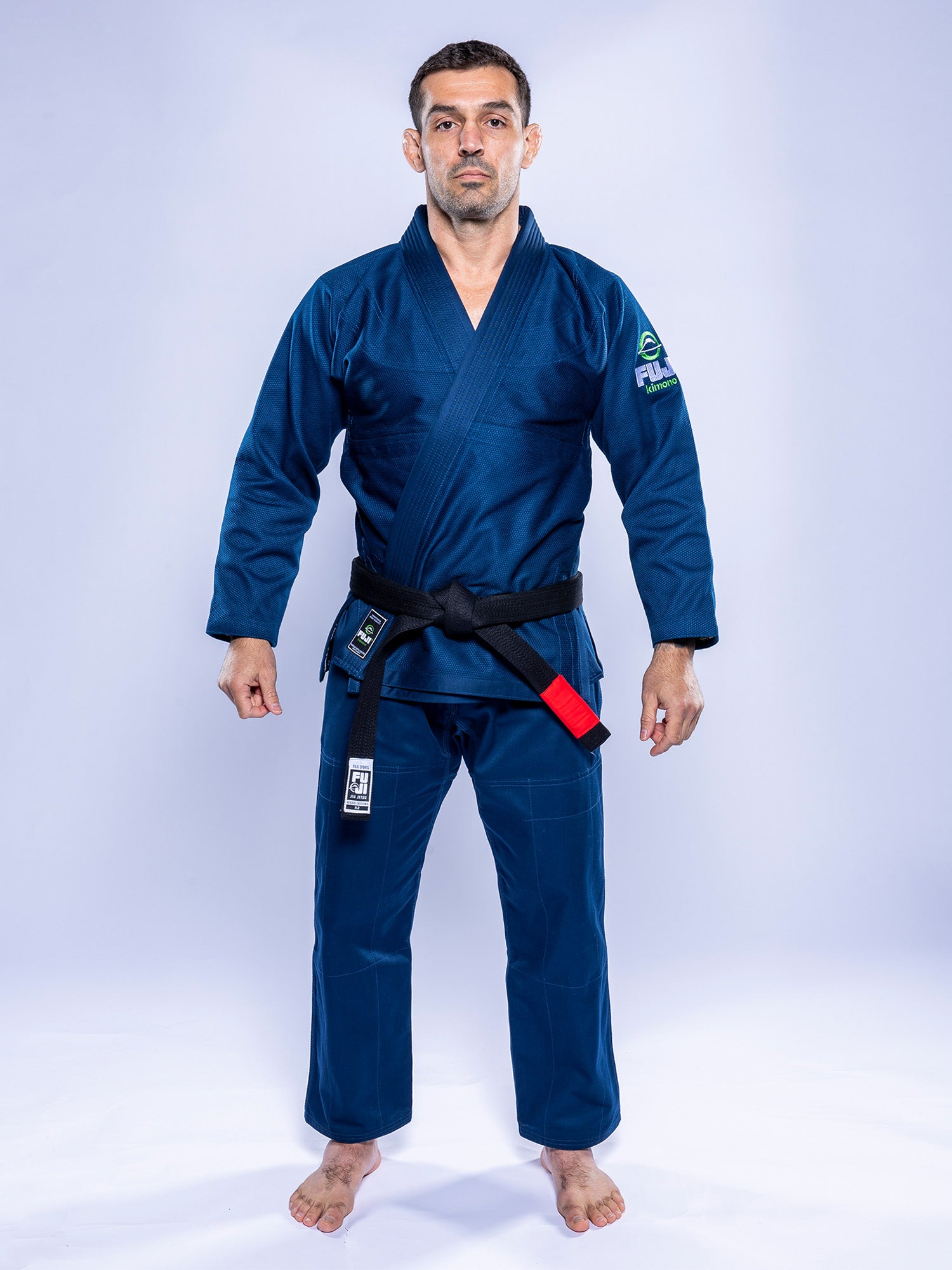 A man wears the Lightweight BJJ Gi Navy with a black belt, standing barefoot on a white background, facing forward with arms relaxed at his sides.