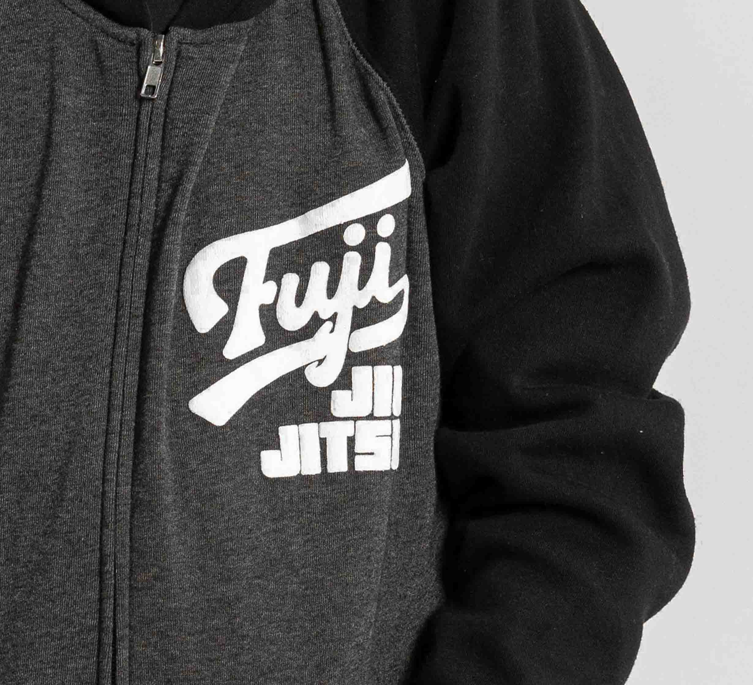 Close-up of a child wearing the Kids Jiu Jitsu Varsity Zip Hoodie in charcoal, featuring "Fuji Jiu Jitsu" in white text on the left chest; only the upper body is shown.