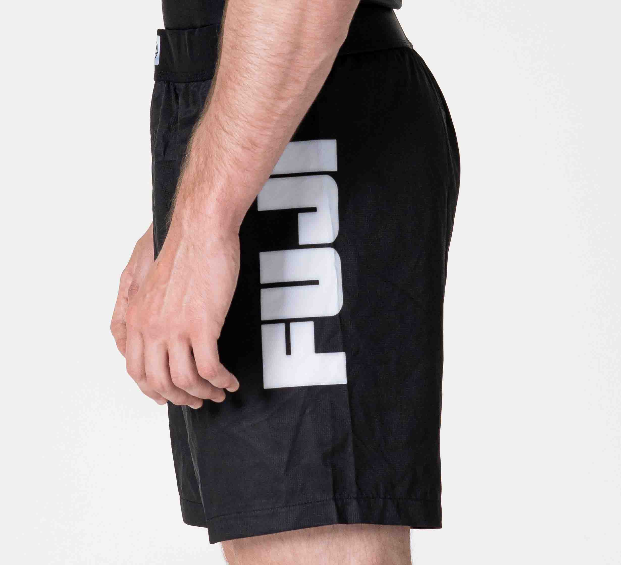 A person is wearing Competition Ranked Shorts Black, featuring "FUJI" printed vertically in large white letters on the left side, standing sideways with their left arm relaxed.