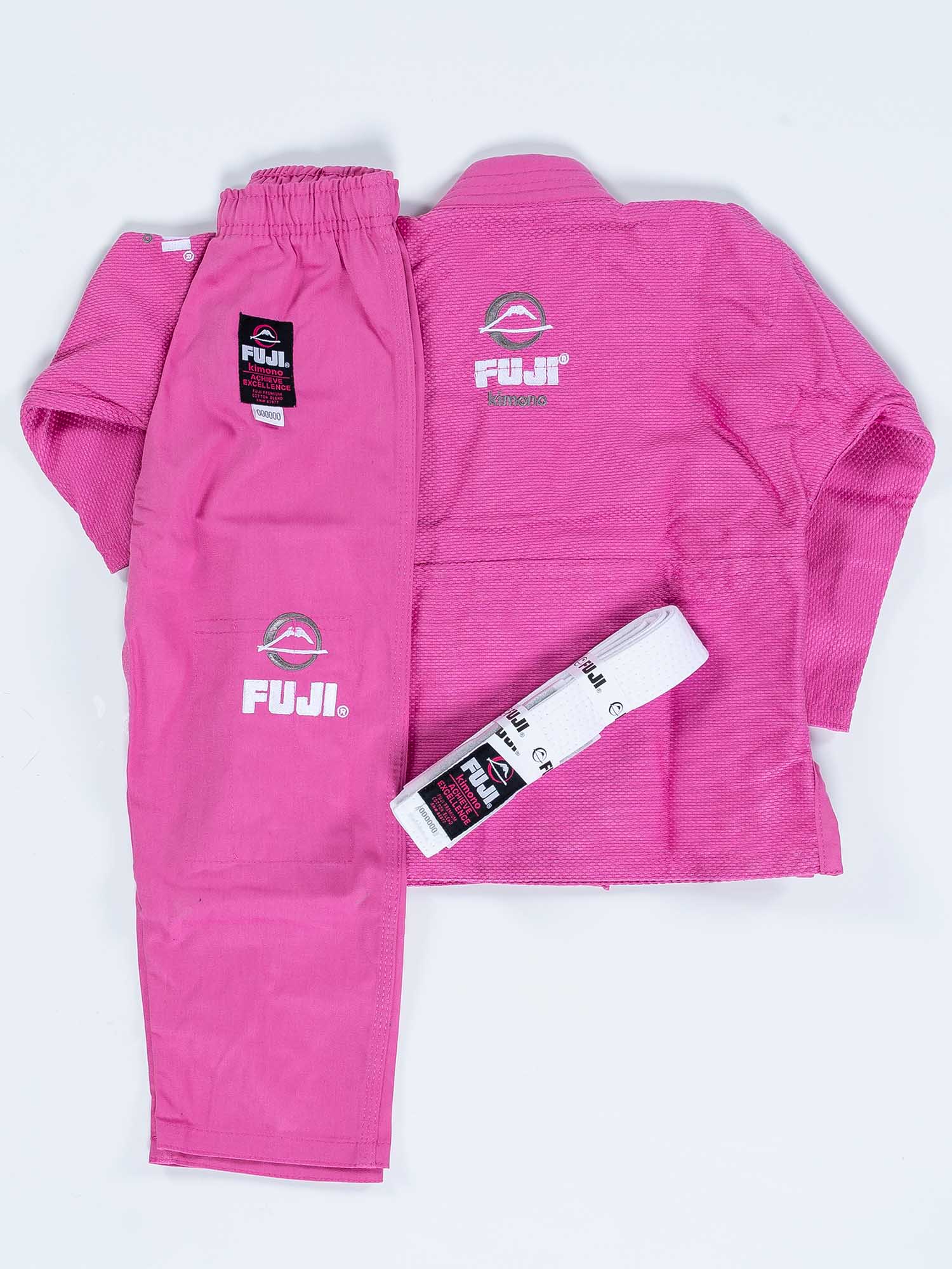 The FUJI Baby Judo Gi set, shown on a white background, includes a pink jacket, pants, and a folded white belt. The gi displays Fuji logos and patches.