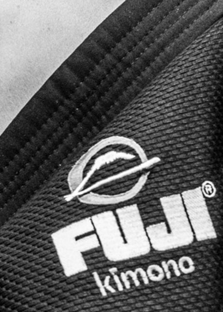 Close-up of a black fabric with white embroidered text reading FUJI kimono and a circular mountain logo above the text. The texture and stitching of the material are clearly visible.