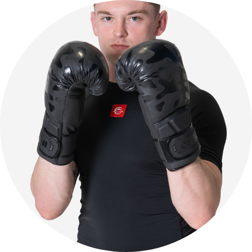A man wearing a black shirt and black camouflage boxing gloves stands in a boxing stance with both fists raised in front of his face.