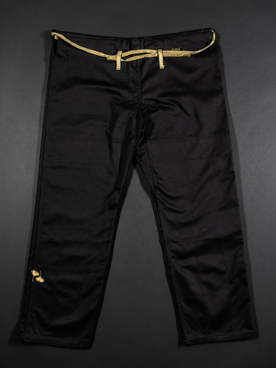 A Womens Heritage Keisho Lightweight BJJ Gi in black, featuring a yellow drawstring and a small yellow patch on the left leg, displayed on a dark background.