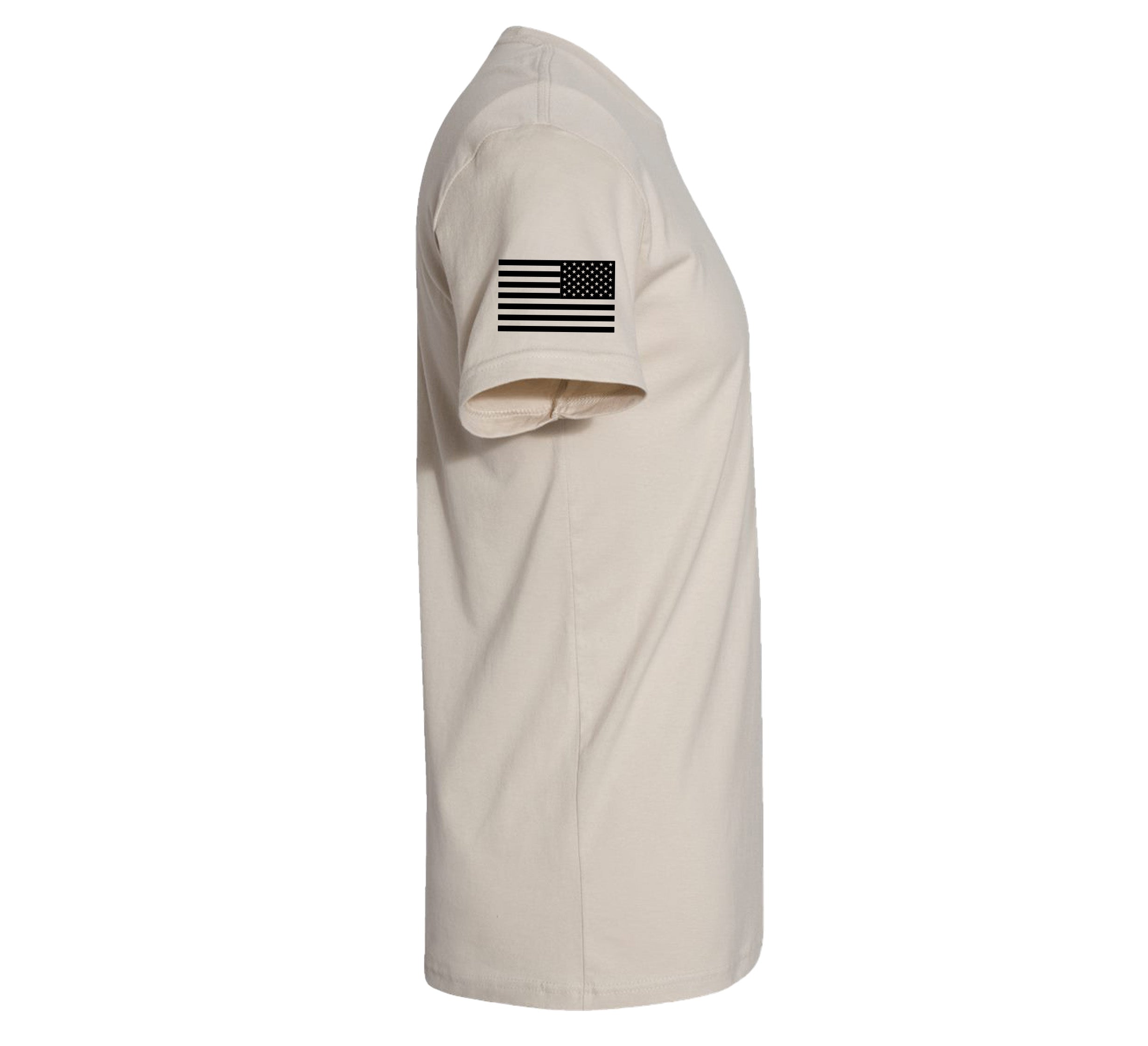 The We Defy Core T-Shirt Sand is a light beige short-sleeve tee shown from the side, featuring a small black and white American flag on the upper sleeve.