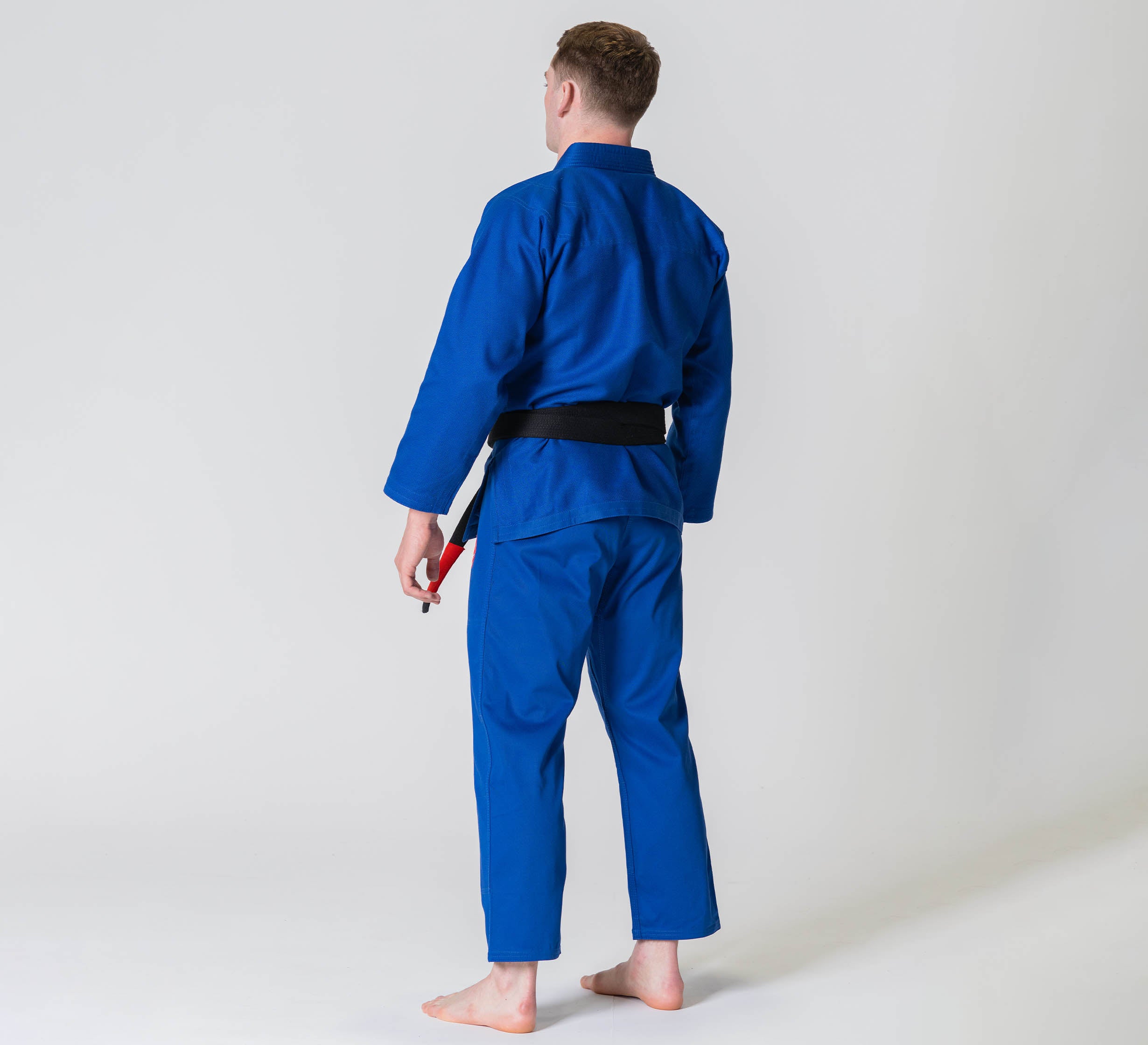 A person wearing the Competition BJJ Gi Blue stands barefoot on a white background, facing away from the camera.