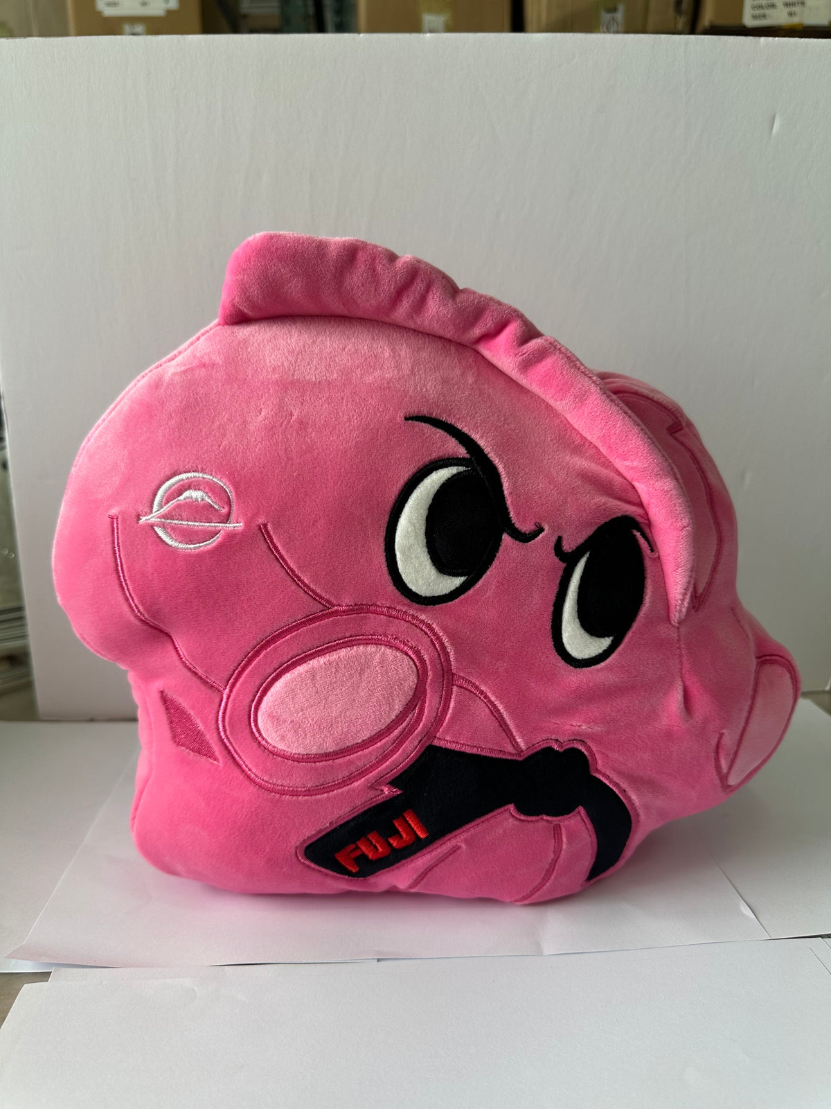 Pochi Piro Pillow Pink is a cloud-shaped pink plush toy with angry eyes, a swirl of hair, and “FUJI” on its black glove, shown against a plain white background.