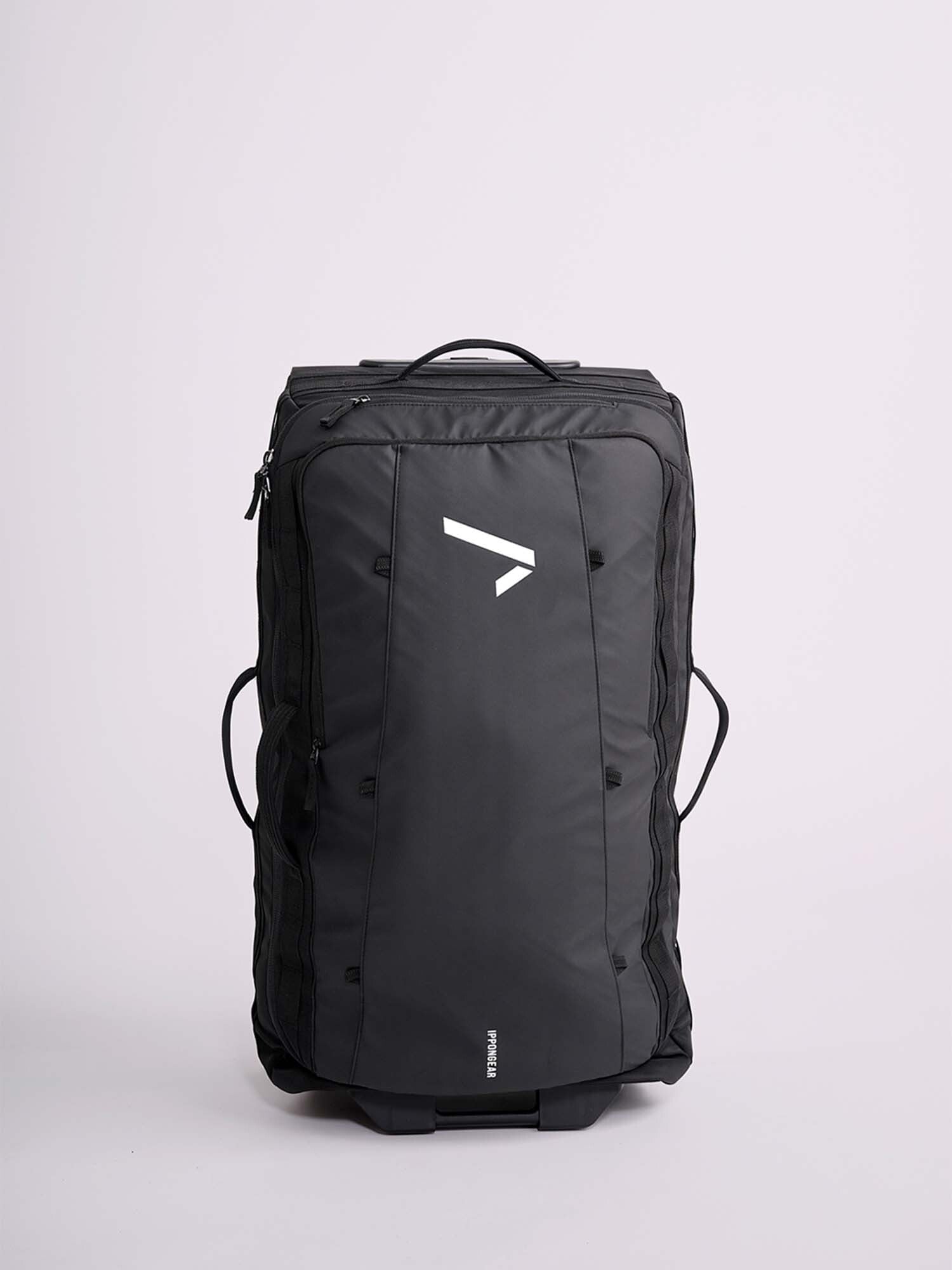 The IPPONGEAR Travel Trolley Black L is a large black duffel with side and top handles, base wheels, and a white angular front logo, shown upright against a plain light background.