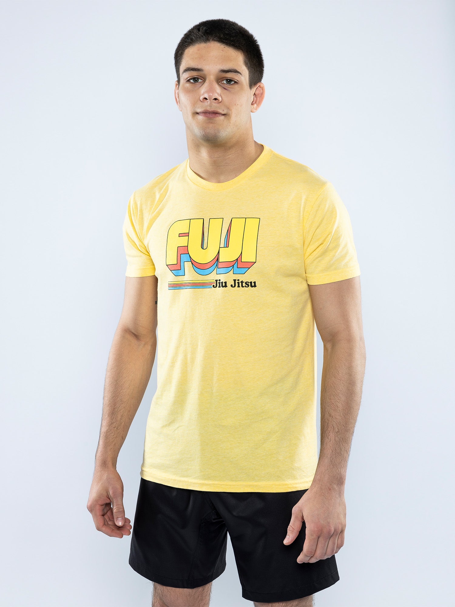 A man stands against a plain light background, wearing a Vintage Jiu Jitsu T-Shirt Yellow and black shorts, looking at the camera with a neutral expression.