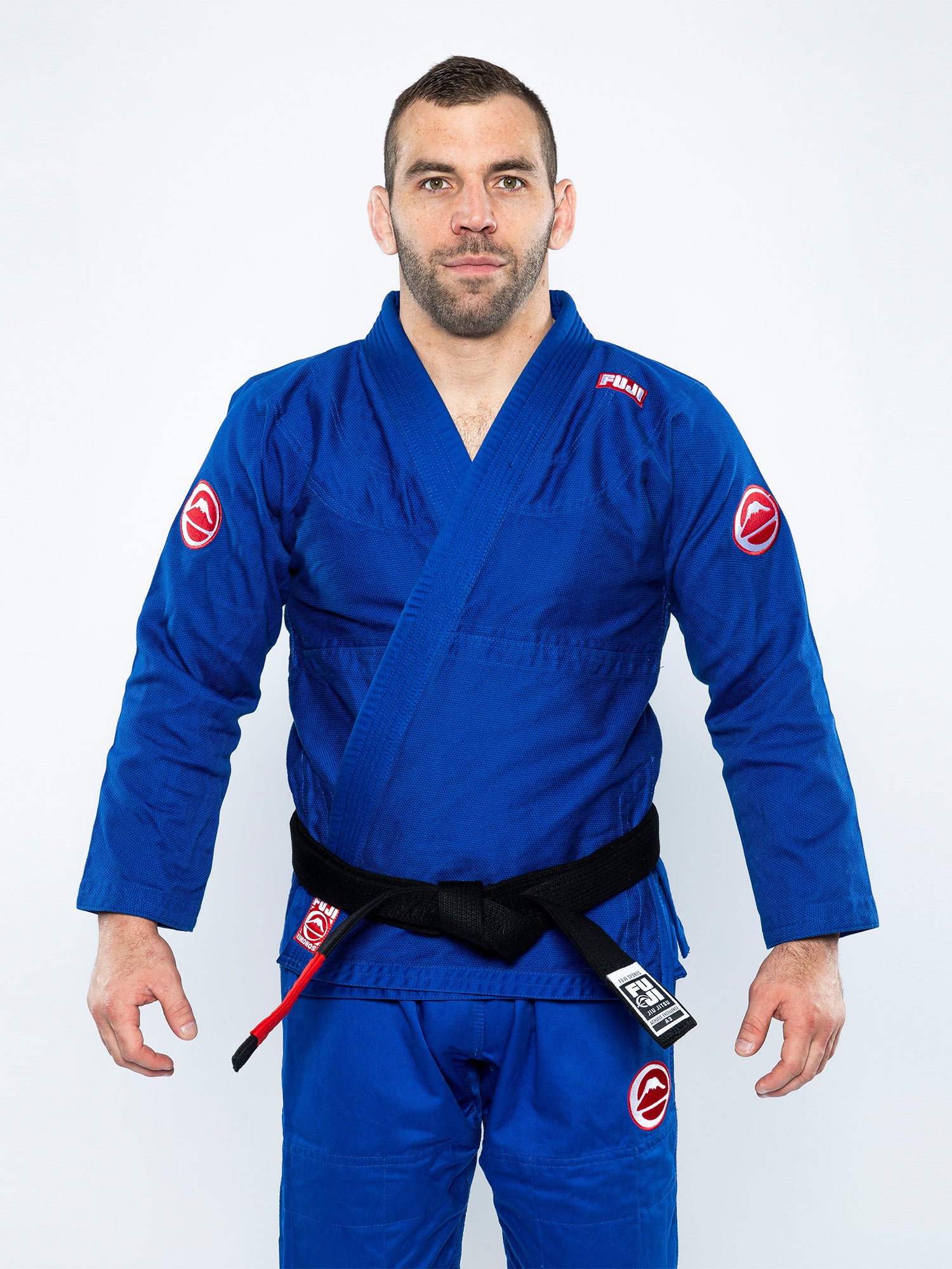 A man stands against a plain white background wearing the Competition BJJ Gi Blue with a black belt, looking directly at the camera with a neutral expression.