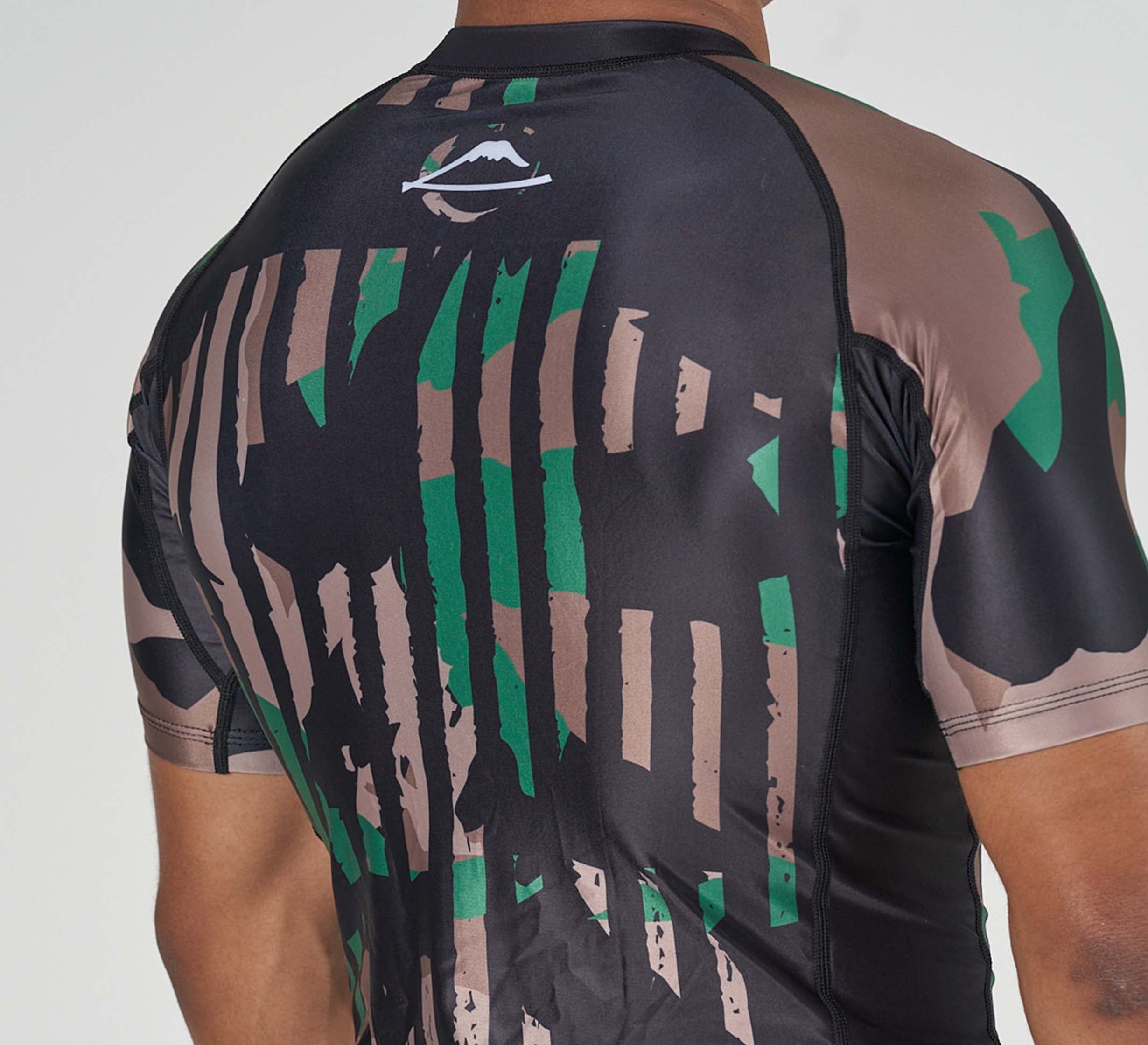 Close-up of a person's back wearing the Camo Flex Lite Rashguard, a fitted short-sleeve athletic shirt with a black, brown, and green camo pattern and a white mountain logo near the collar.