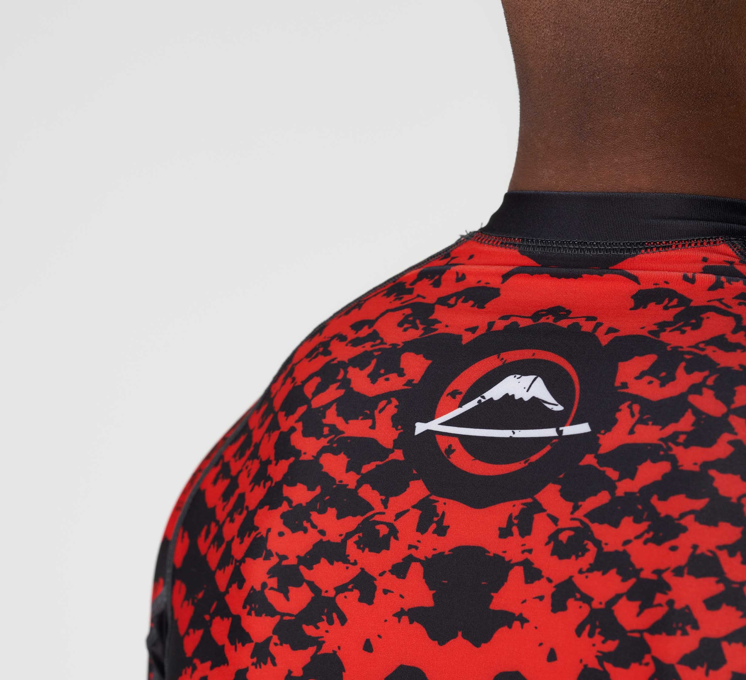Close-up of a person wearing the Oni vs. Anaconda Short Sleeve Rashguard Red, featuring a white mountain logo inside a circle on the upper back. Only the shoulder and neck area are shown.