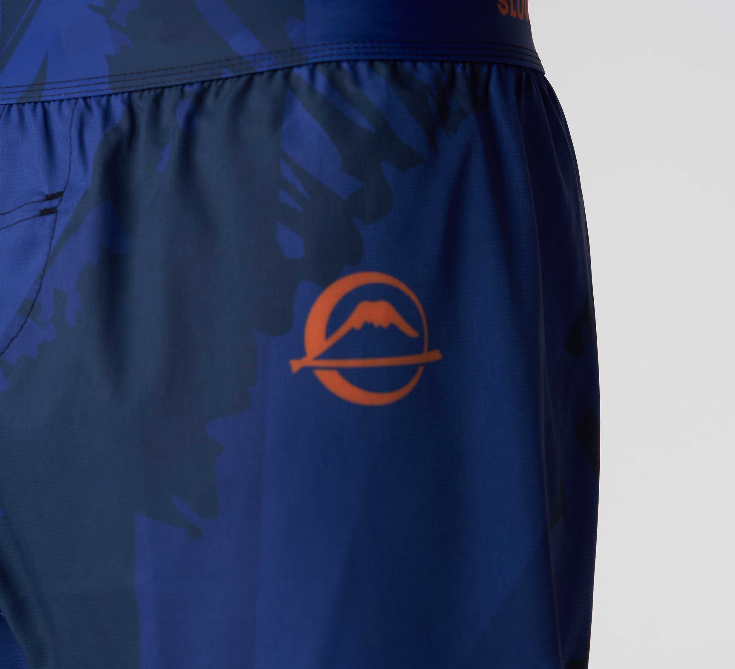 Close-up of Hanzo Flex Lite Shorts Blue with an orange circular mountain logo on the left thigh.