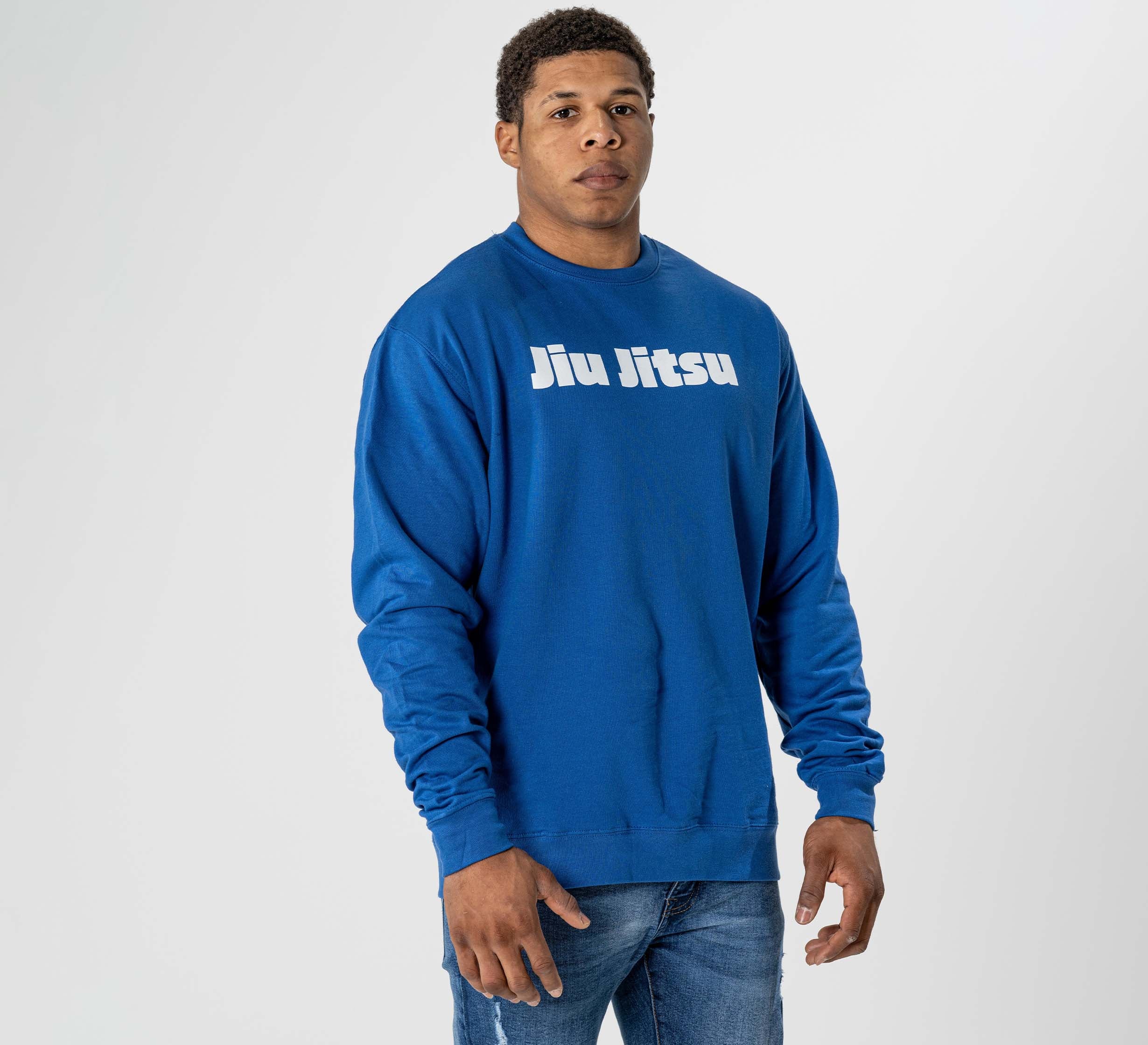 A man faces the camera with a neutral expression, wearing the Jiu Jitsu Player Crewneck Blue sweatshirt featuring white "Jiu Jitsu" text, standing against a plain white background.