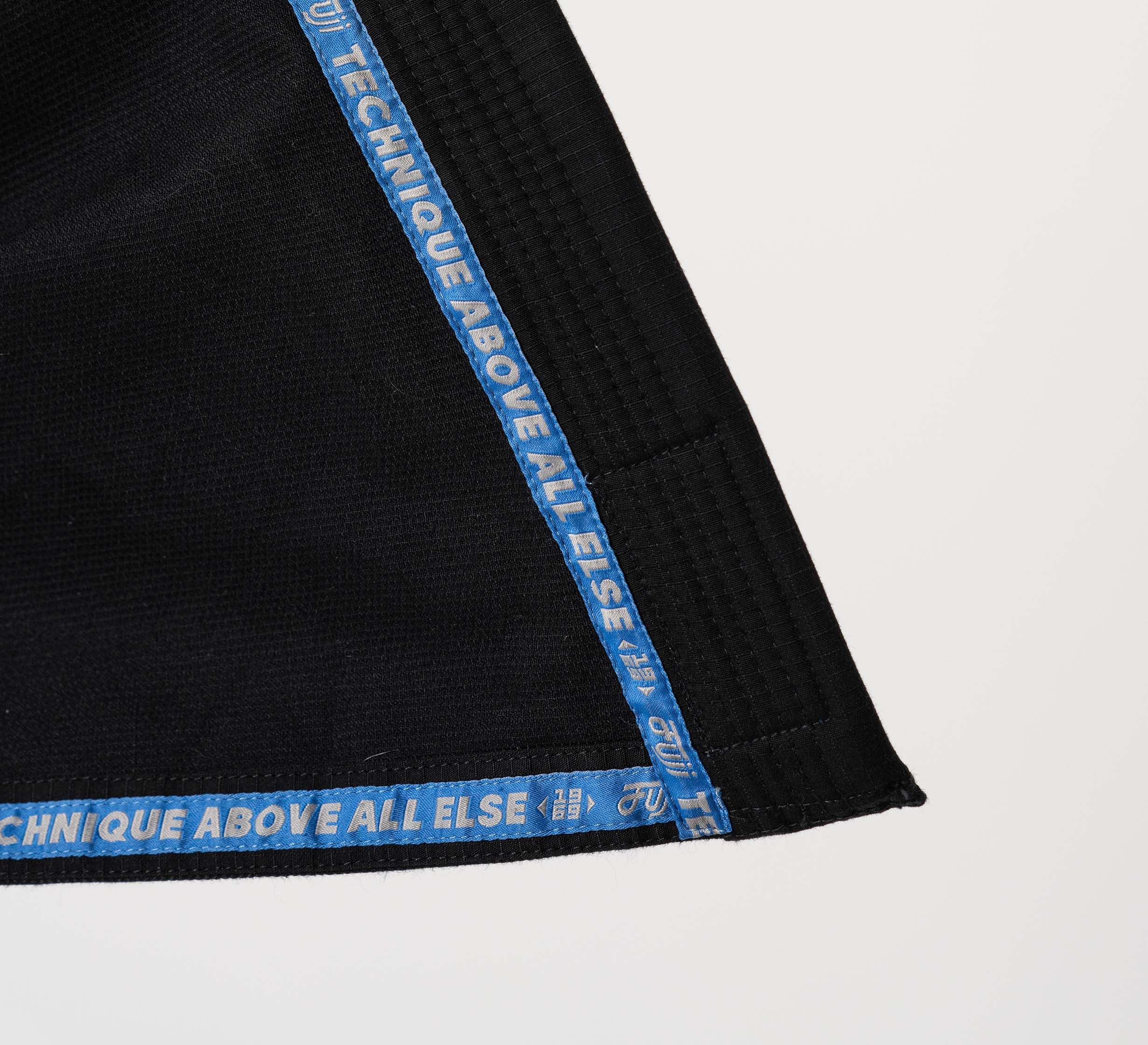 A close-up of the Flow-Tech BJJ Gi in black with blue trim and “TECHNIQUE ABOVE ALL ELSE” in white lettering on a plain white background.