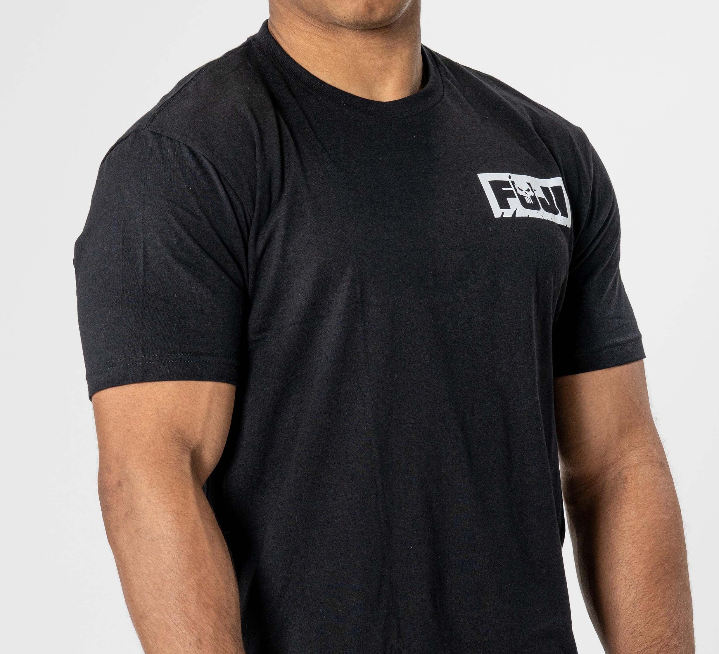 A person wearing the Punishment T-Shirt Black, a fitted black tee with a small white logo on the left chest, stands against a plain white background. Their head is partially out of frame.