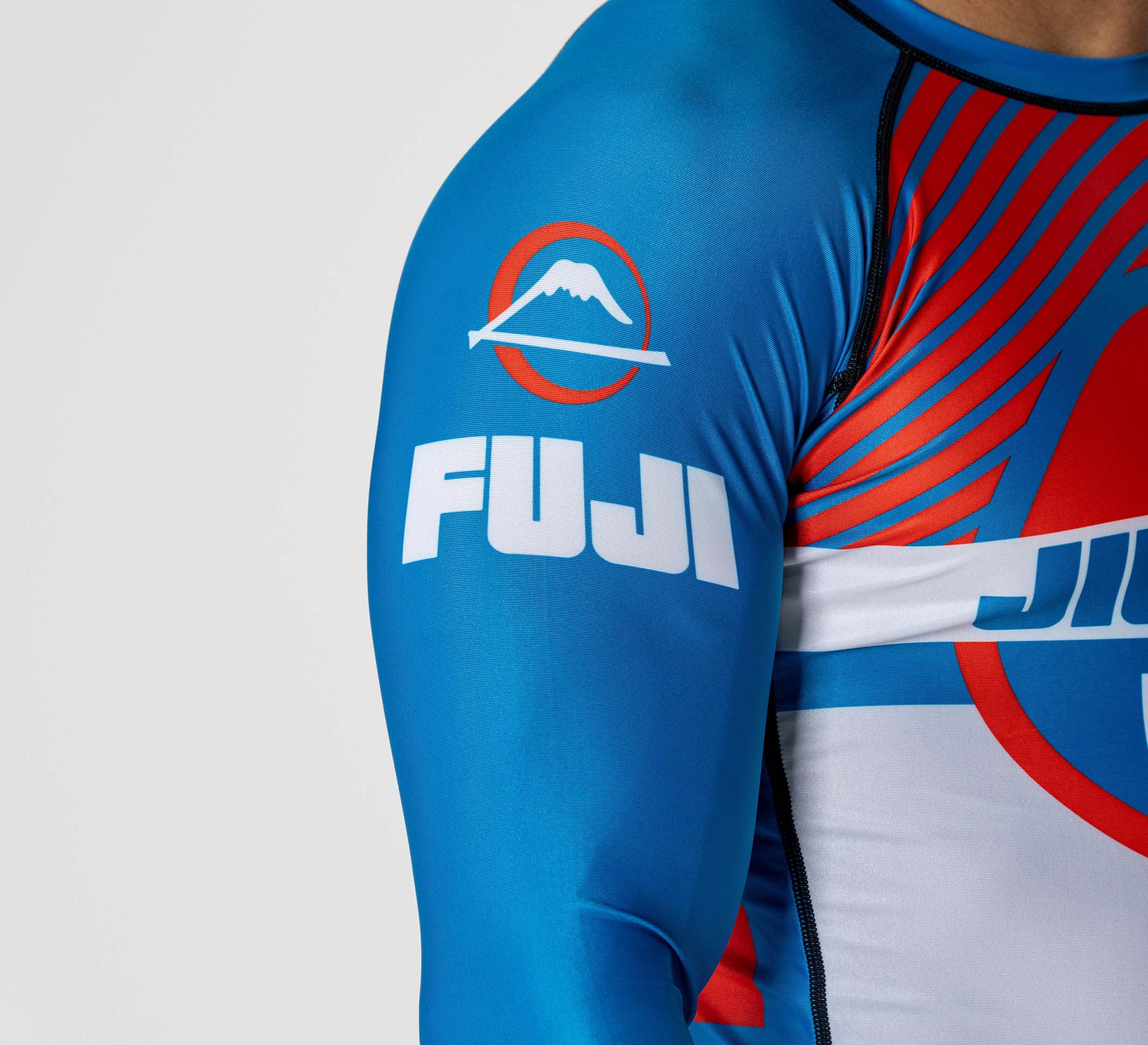 A close-up of a person wearing the Pacer Flex Lite Long Sleeve Rashguard Blue/Red, featuring a FUJI mountain logo on the sleeve and red and blue abstract designs on the front.