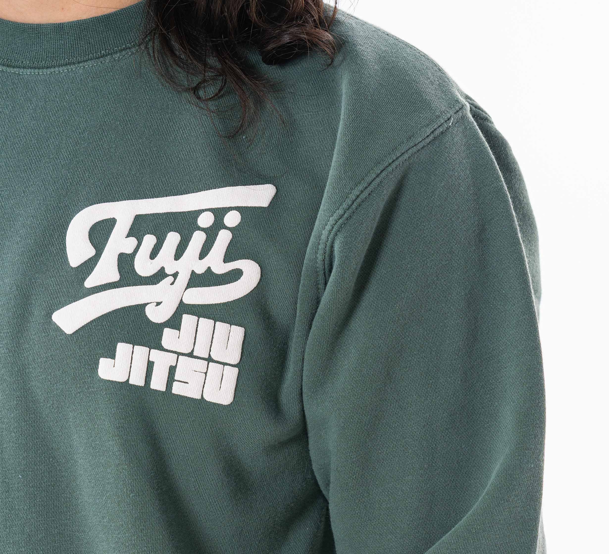 Close-up of a person wearing the Women's Signature Crewneck Green sweatshirt, featuring white "Fuji Jiu Jitsu" text on the upper left chest. The person's long dark hair is partially visible.
