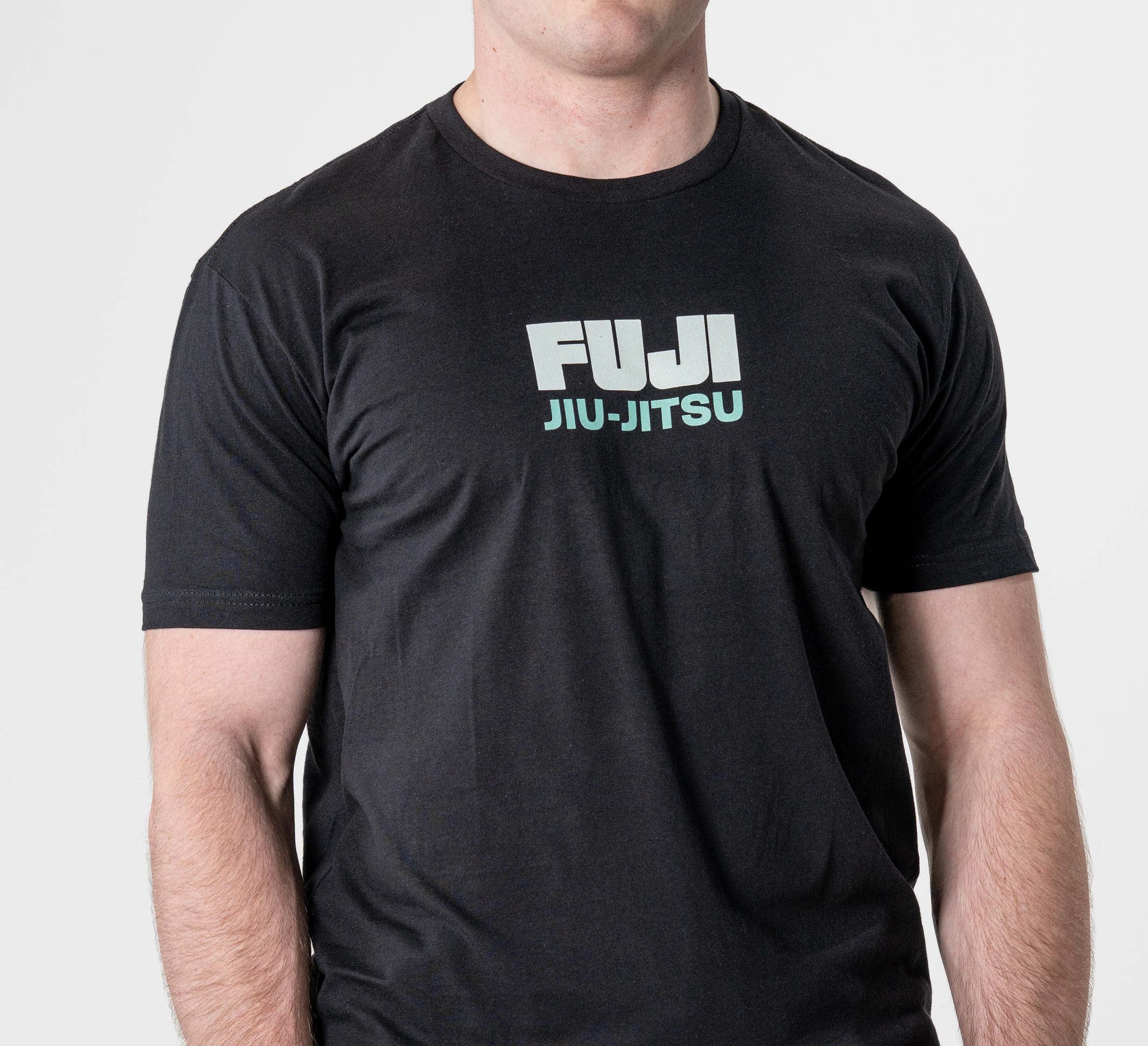 A man wears the Black Belt Mentality T-Shirt Black, featuring "FUJI JIU-JITSU" in white and light blue on the chest, standing against a plain white background.