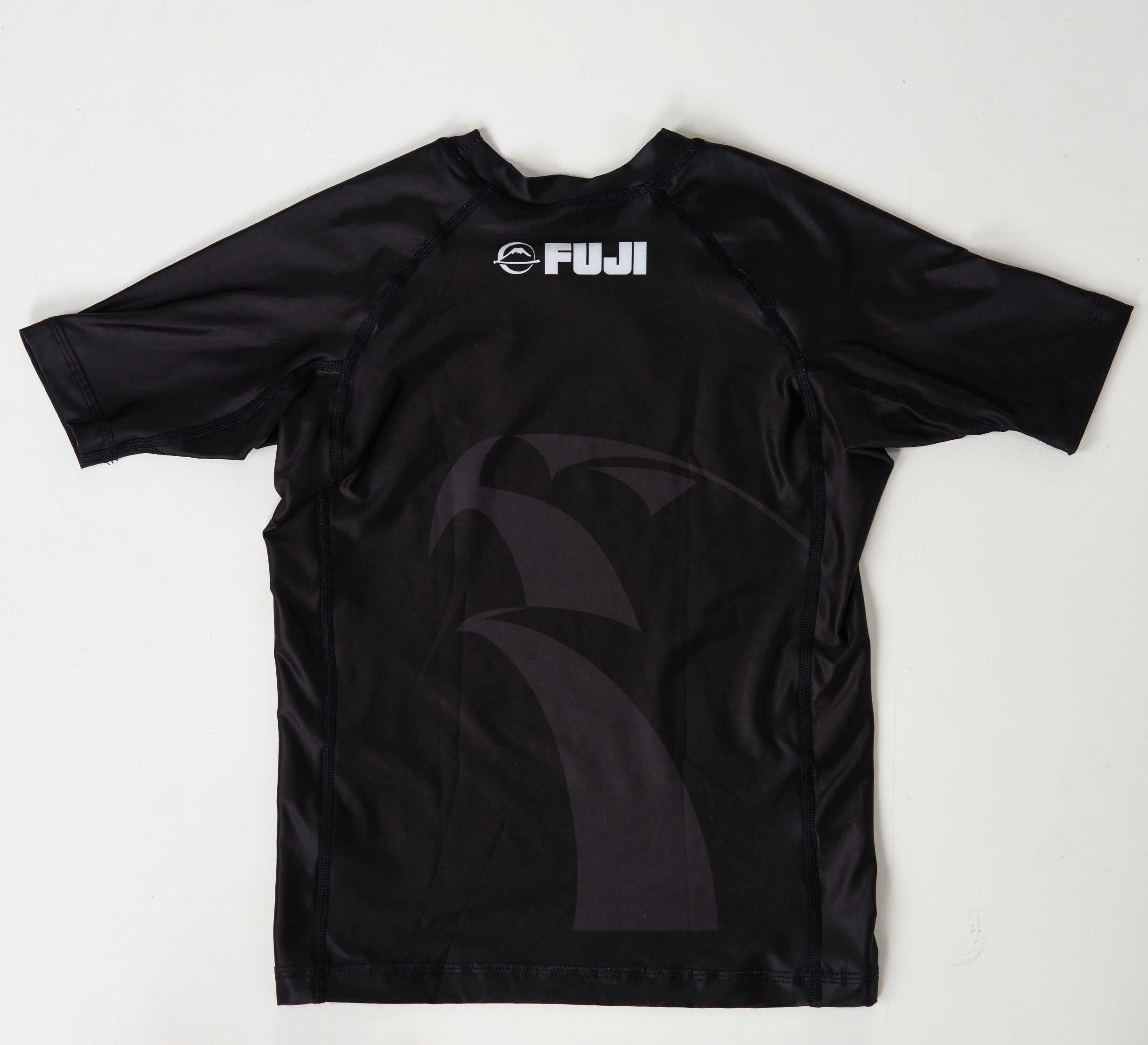 The Kids FUJI x Alliance Ranked Short Sleeve Rashguard Black features "FUJI" and a white circular logo printed on the upper back, subtle dark patterns, short sleeves, and is shown on a white background.