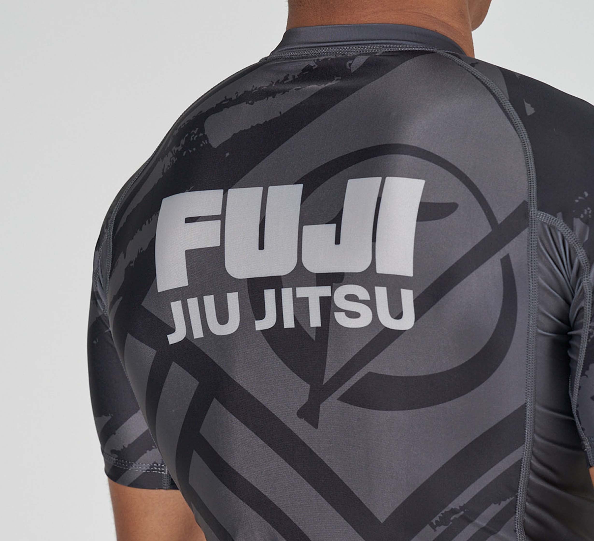 A person wearing the Battle Flex Lite Rashguard Black, featuring bold white "FUJI JIU JITSU" lettering and a stylized mountain logo on the back. The photo shows the view from behind.