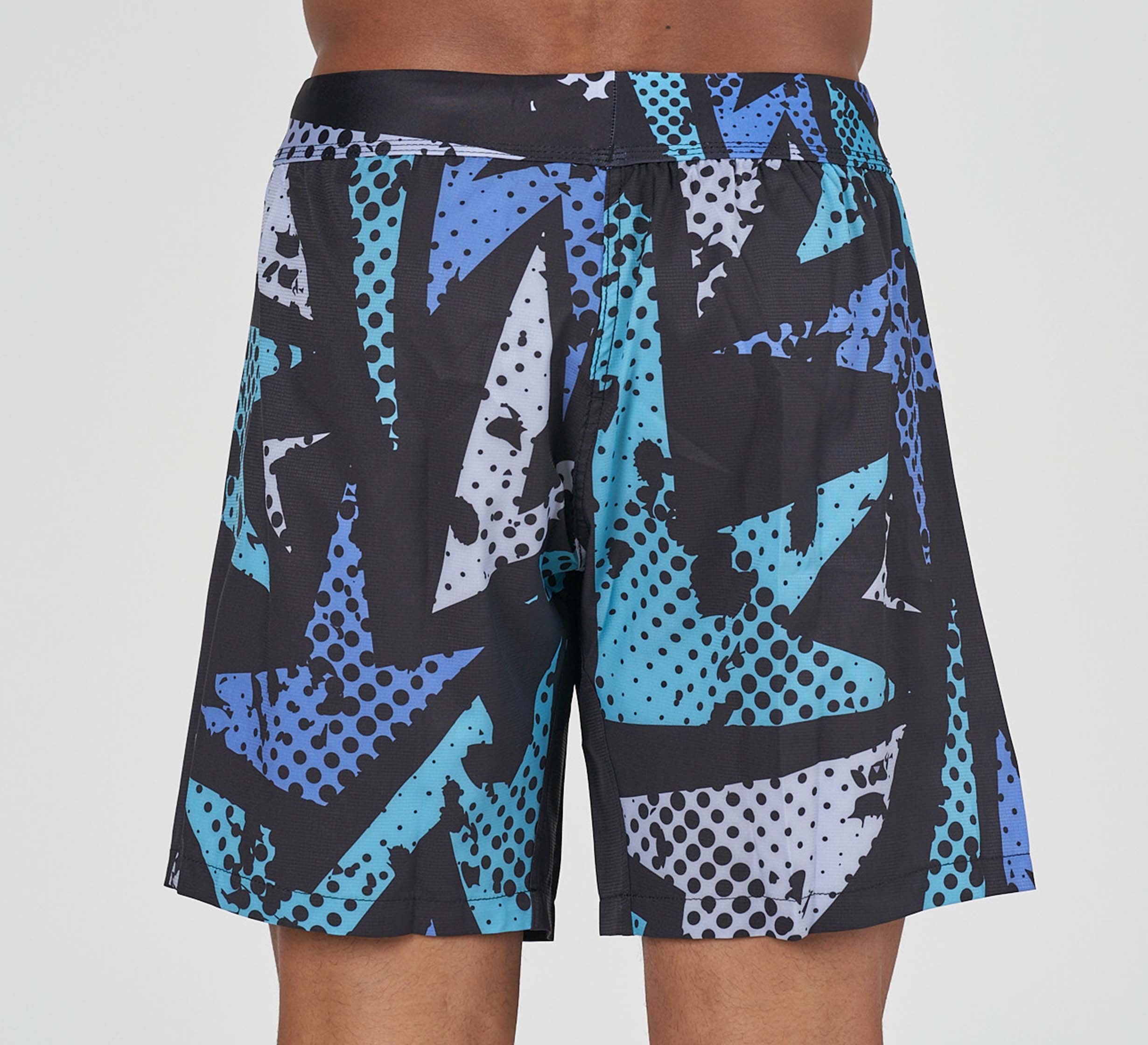 A person models the Shuriken Flex Lite Shorts Blue/Purple, knee-length with an abstract geometric blue, black, and white design featuring polka dots and jagged shapes. The image highlights the back view of the shorts.
