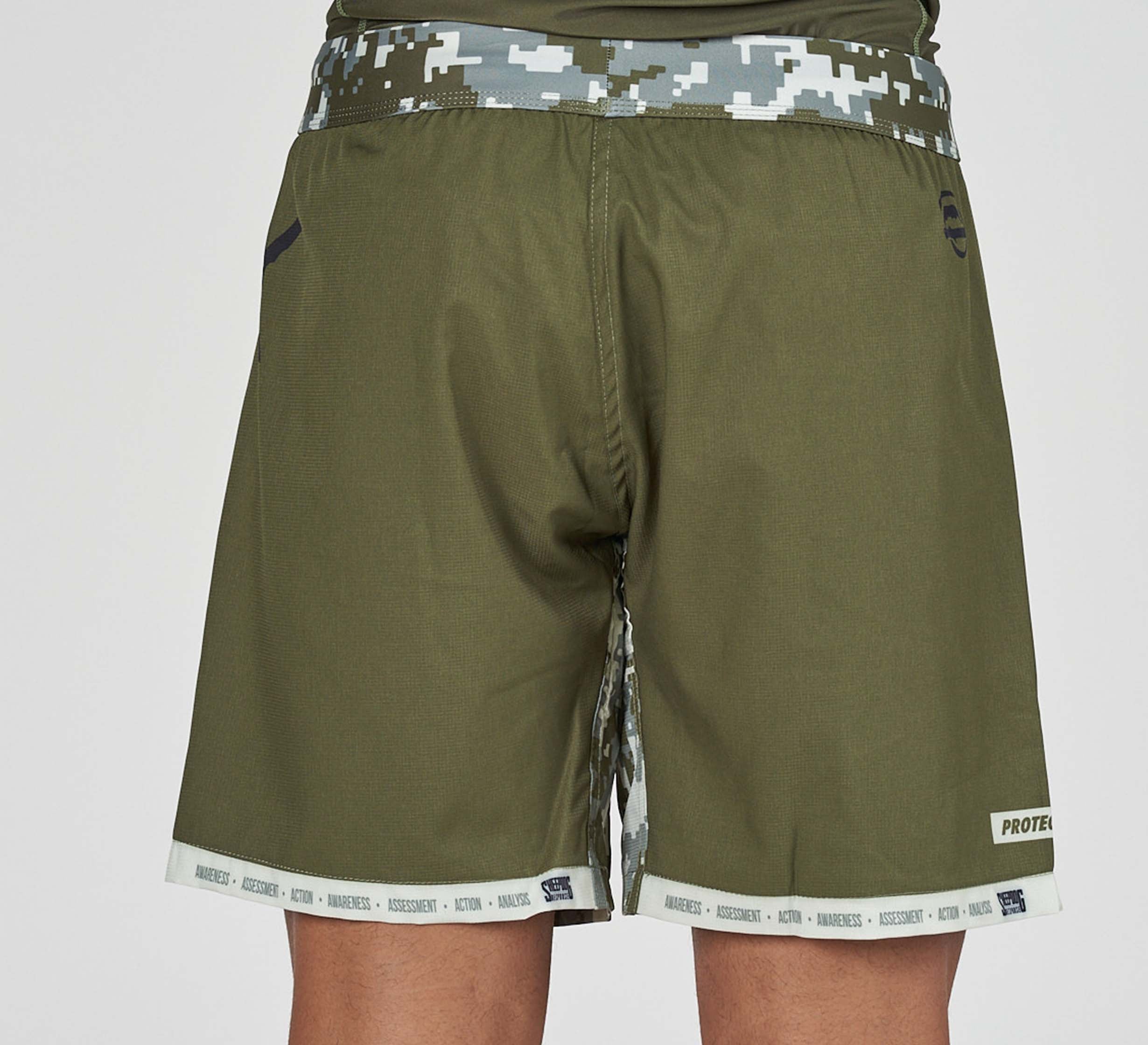 A person is seen from the back wearing Sheepdog Response Flex Lite Shorts in Military Green with a camo-patterned waistband and trim, plus small logo details and text near the bottom hem.