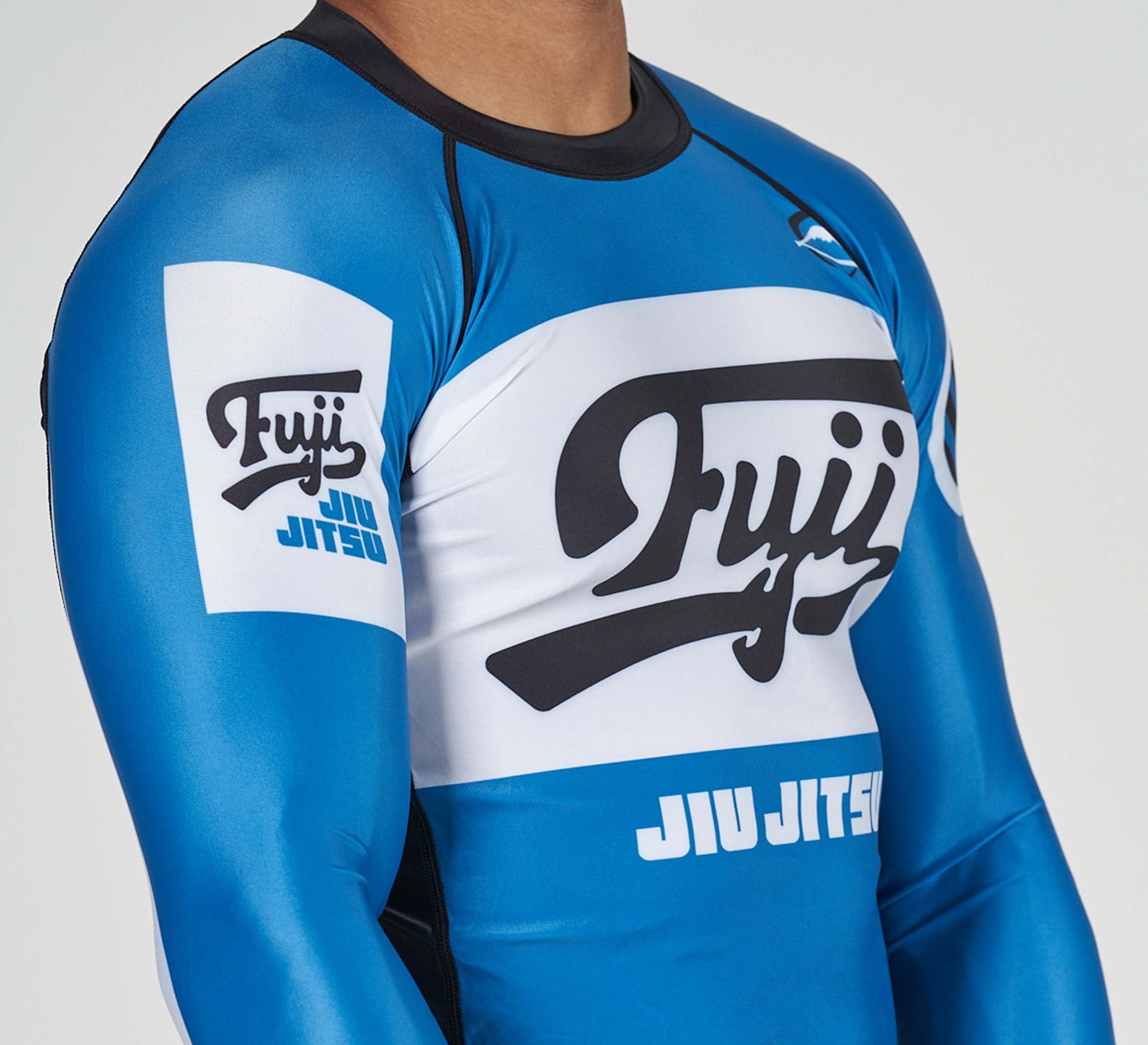 Someone wearing the Jiu Jitsu Script Flex Lite Long Sleeve Rashguard in blue, featuring Jiu Jitsu and Fuji logos on the chest and arm.
