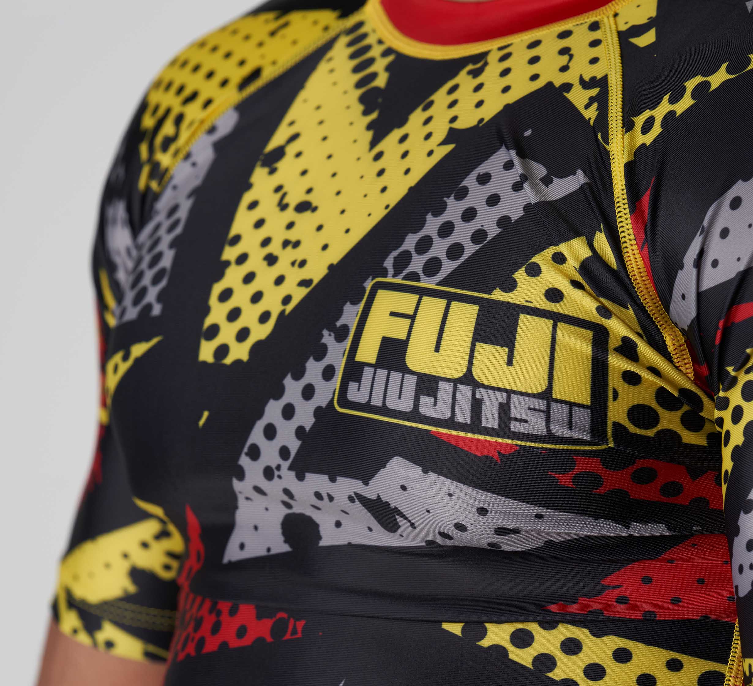 Close-up of a person wearing the Shuriken Flex Lite Rashguard Black/Yellow, featuring a bold graphic design with FUJI Jiu Jitsu logo printed on the chest.