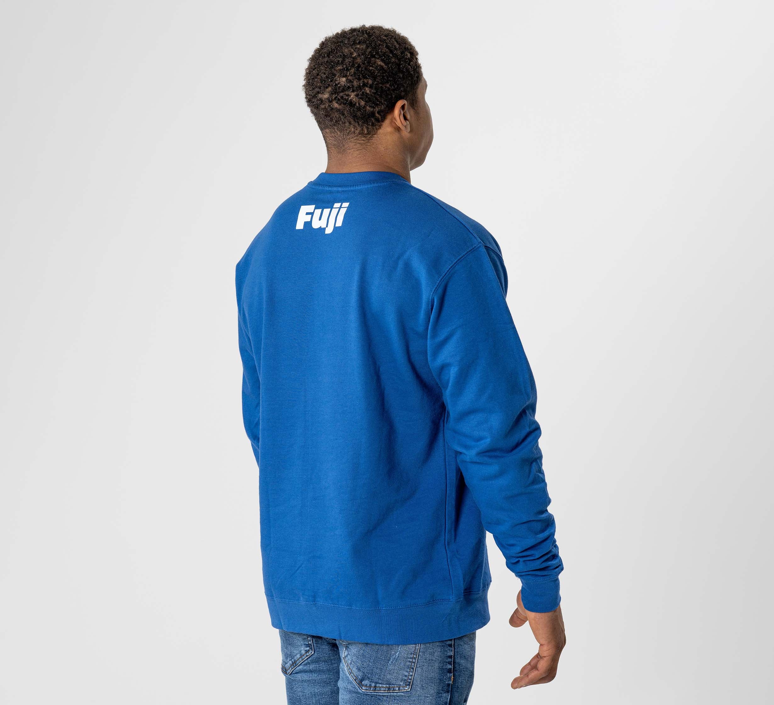 Someone wearing the Jiu Jitsu Player Crewneck Blue, featuring "Fuji" in white text on the back, stands with their back to the camera against a plain light background.