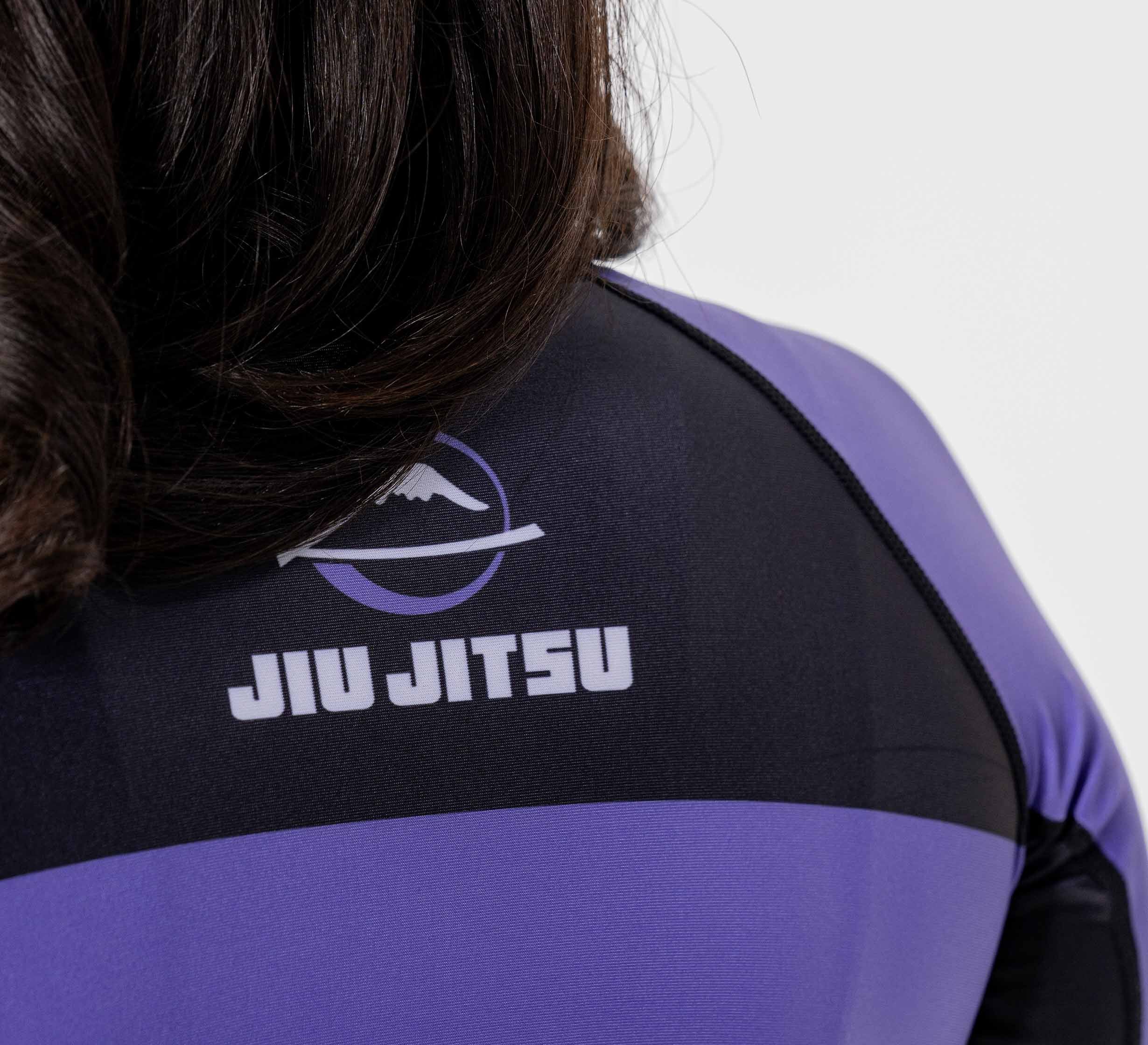 Close-up of a person wearing the Women's Jiu Jitsu Script Flex Lite Long Sleeve Rashguard in purple, featuring a mountain logo and "JIU JITSU" script on the back. The wearer’s hair partially covers the top of the shirt.