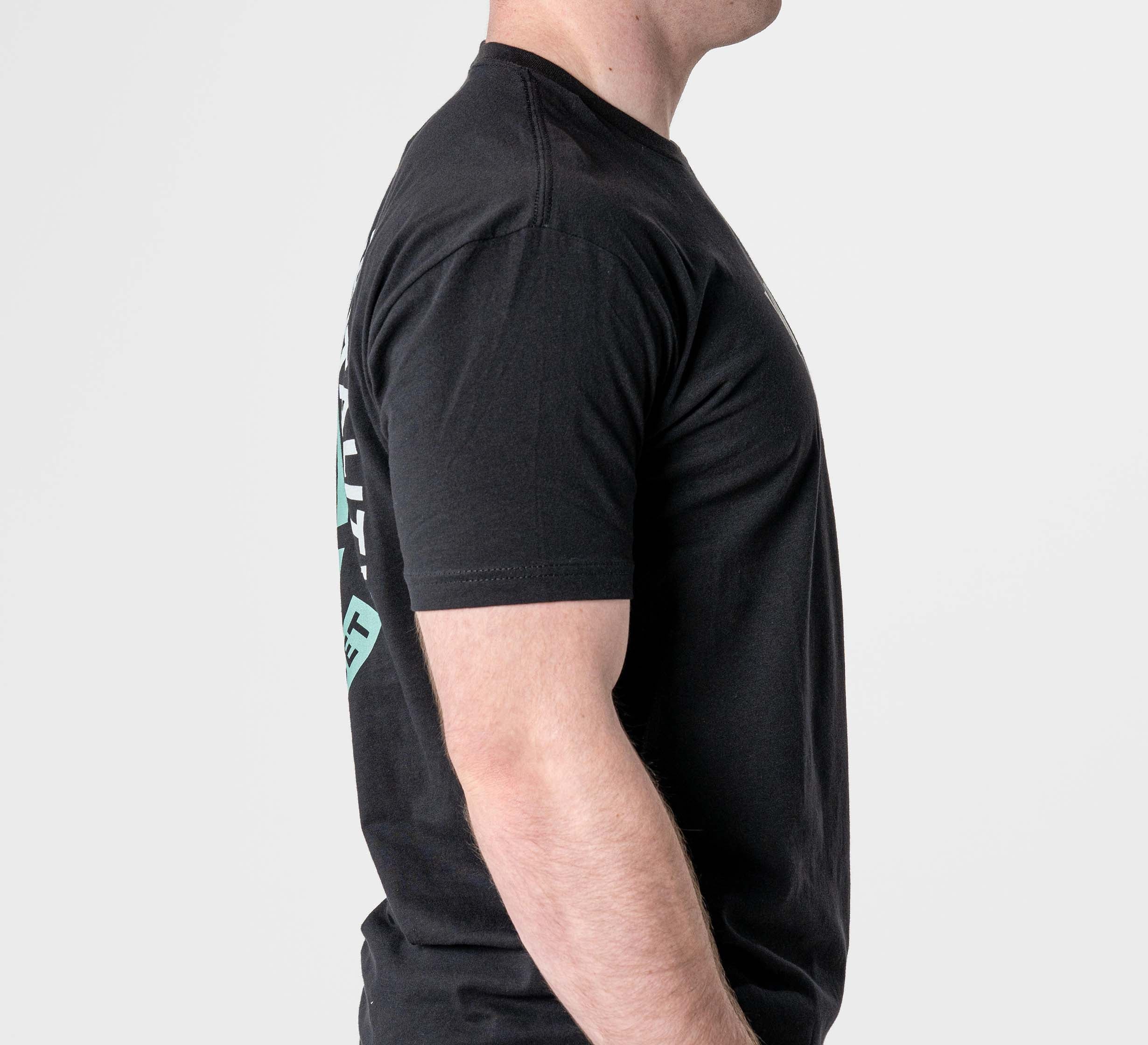 A man stands in profile against a plain white background, wearing the Black Belt Mentality T-Shirt Black with short sleeves and his arms relaxed at his sides.