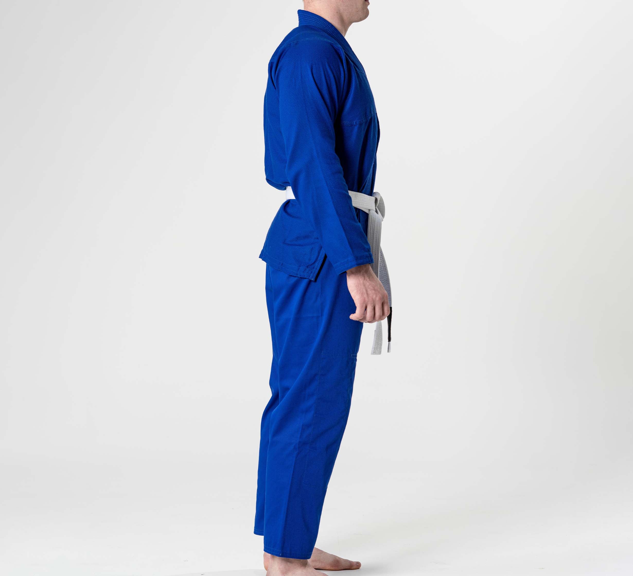 A person stands barefoot in side profile, wearing the Starter Adult BJJ Gi Blue with a white belt, against a plain white background.