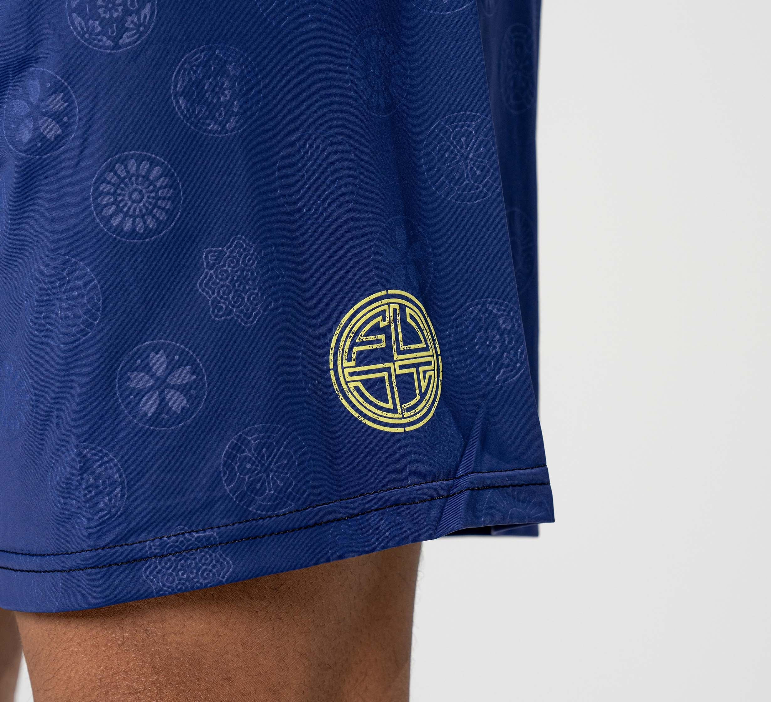 A close-up of a person wearing Shogun Heat Gear Shorts Navy with circular patterns and a yellow emblem near the hem, focusing on the lower thigh area against a plain background.
