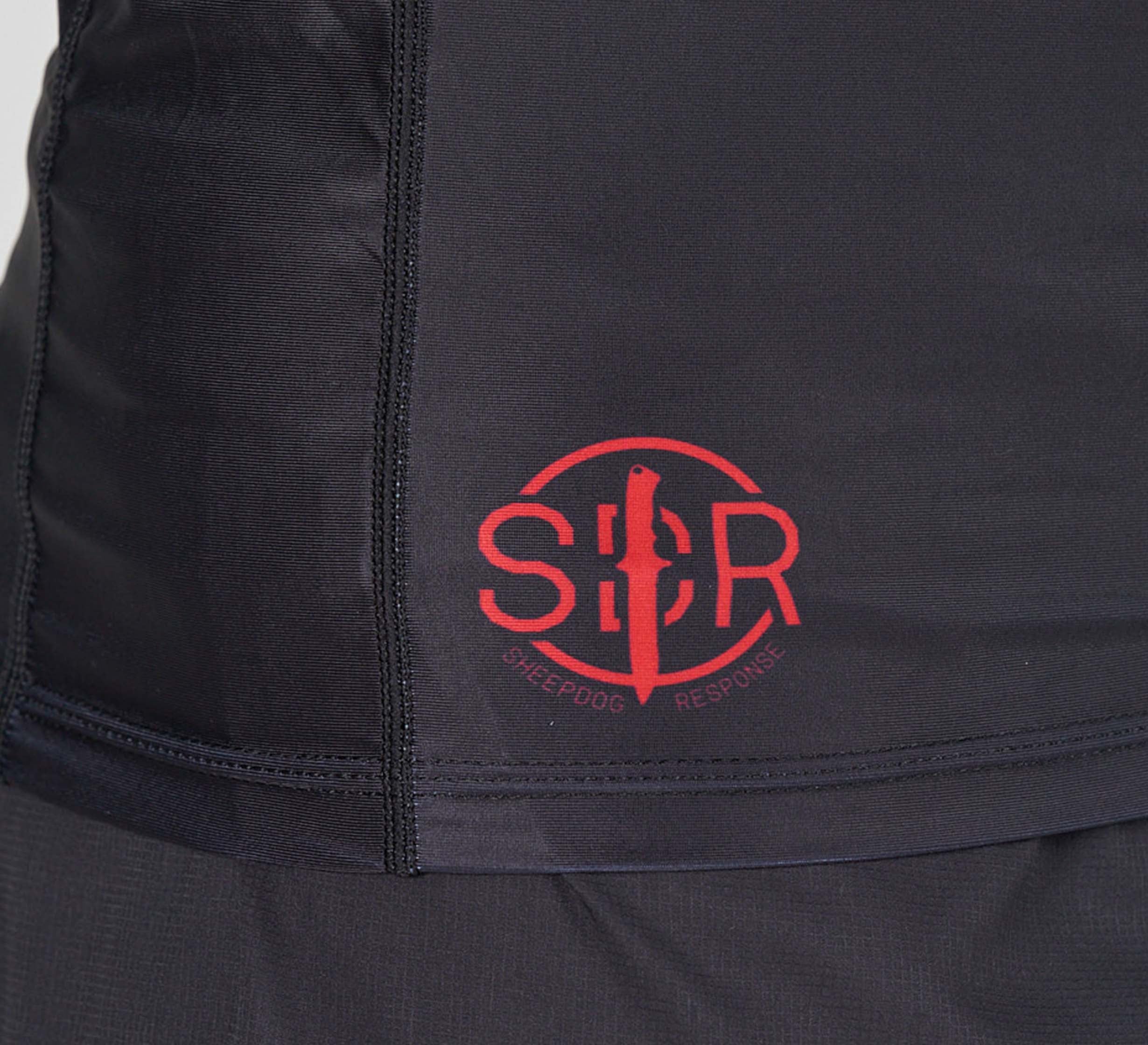 Close-up of the Sheepdog Response Flex Lite Rashguard Black, featuring black athletic fabric with a red SDR logo displaying a dog and person silhouette inside a circle.