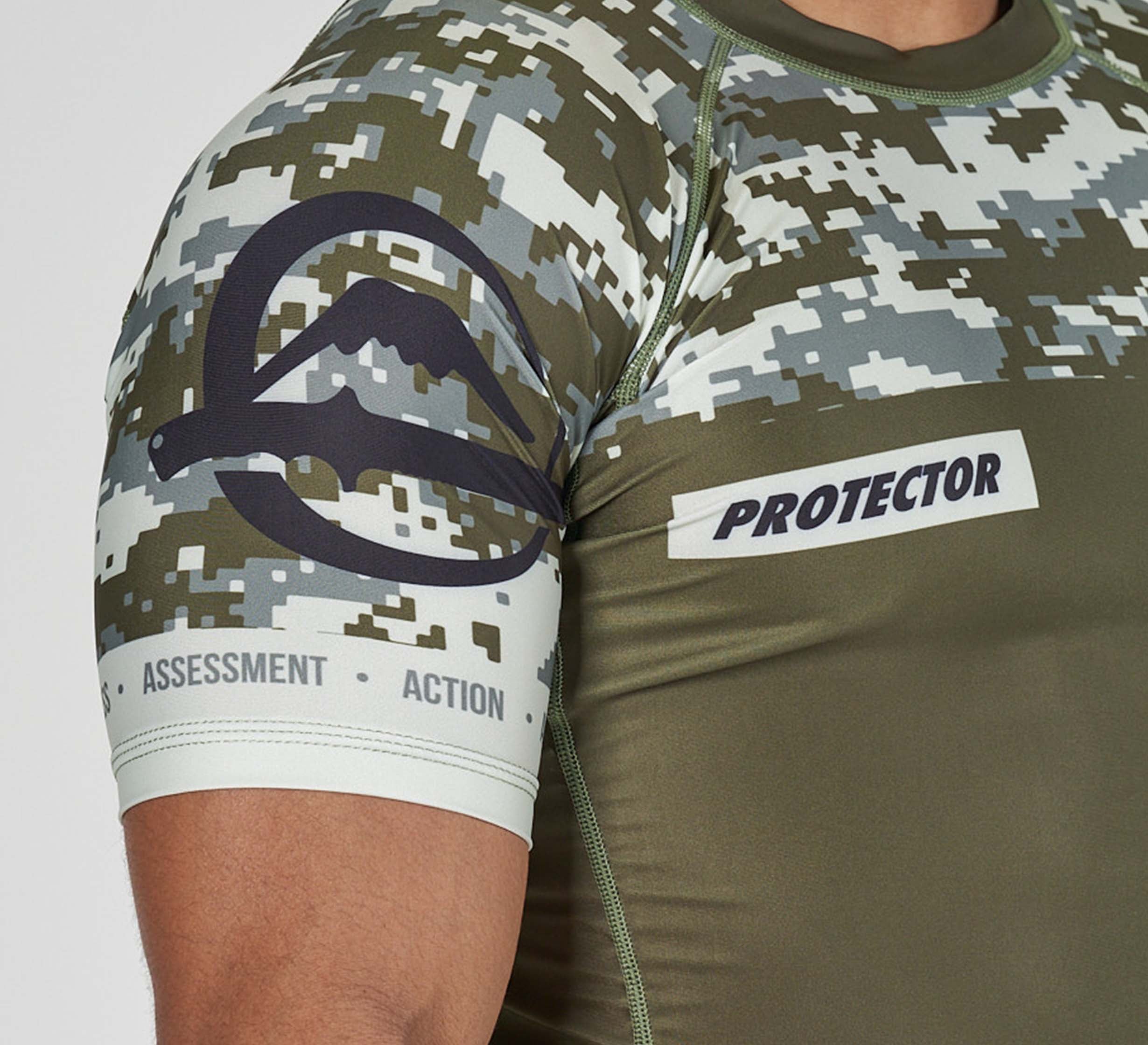 A close-up of a person wearing the Sheepdog Response Flex Lite Rashguard in Military Green, featuring a camouflage pattern, "PROTECTOR" patch, “ASSESSMENT” and “ACTION” text on the sleeve, and a distinctive dark graphic logo.