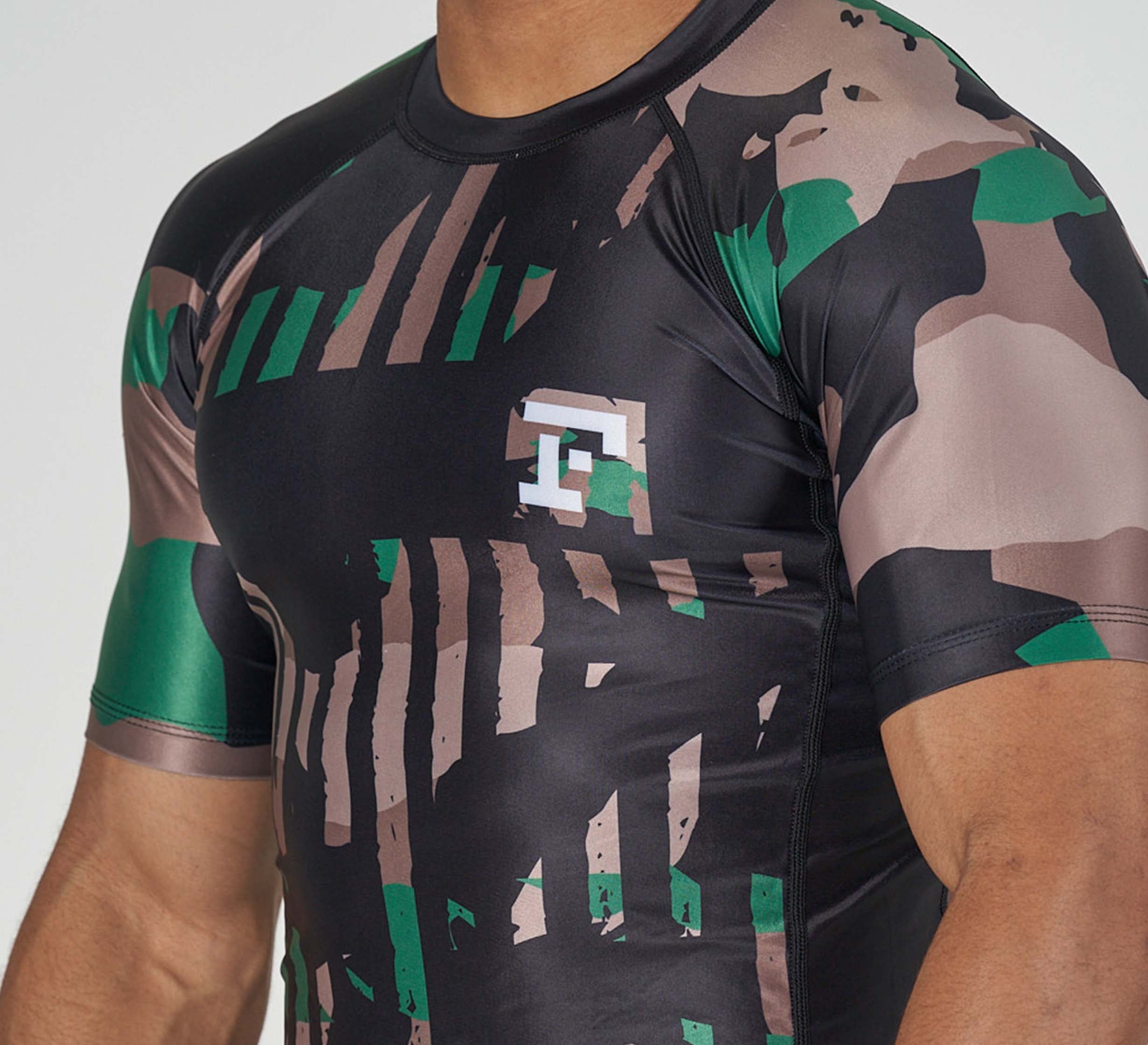 Someone wearing the Camo Flex Lite Rashguard, a fitted short-sleeve athletic shirt featuring a green, black, and brown camouflage pattern with a white T logo on the chest.