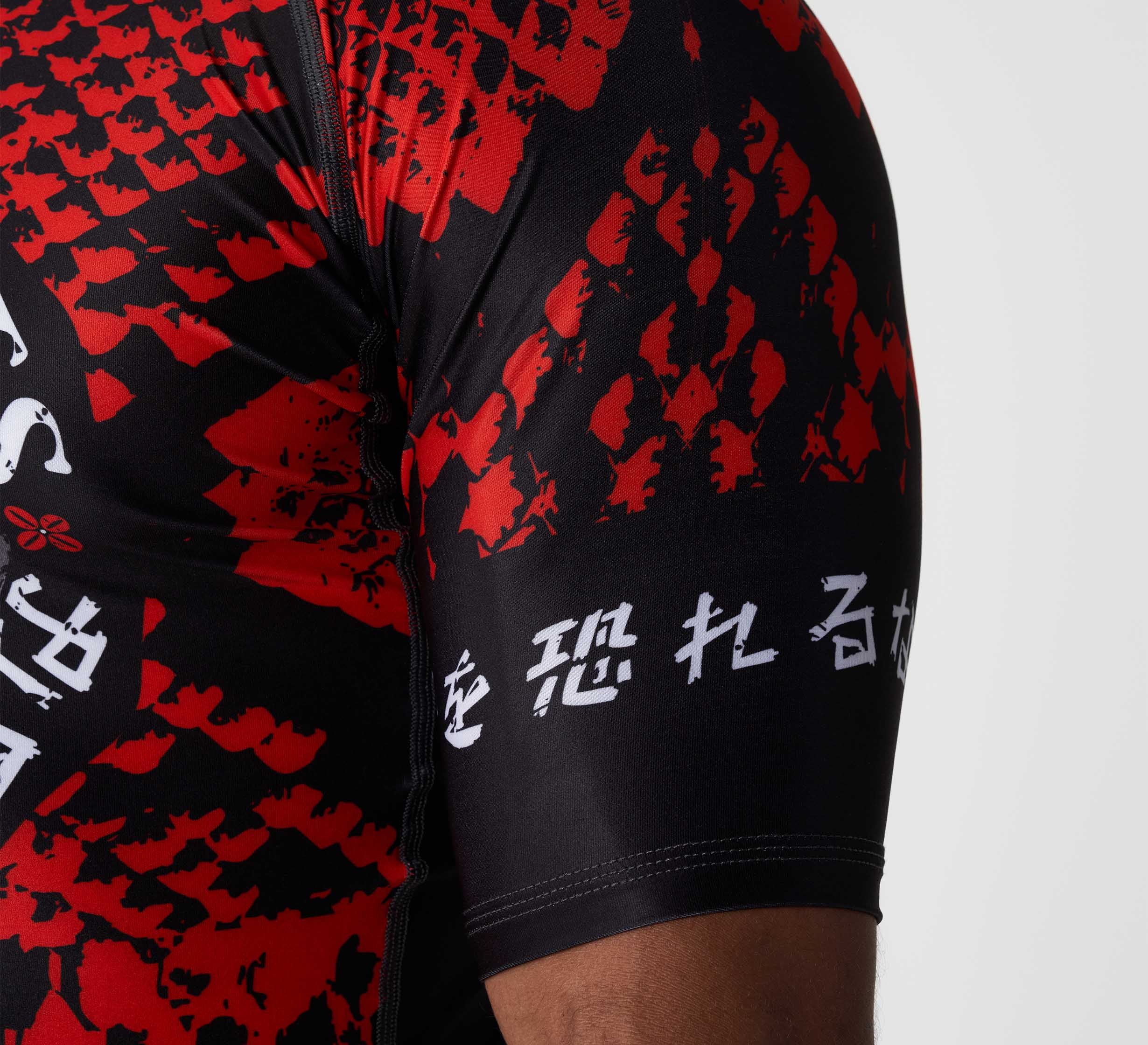 Close-up of a person's arm wearing the Oni vs. Anaconda Short Sleeve Rashguard Red, featuring bold red graphic patterns and white Asian script on the black sleeve against a plain light background.