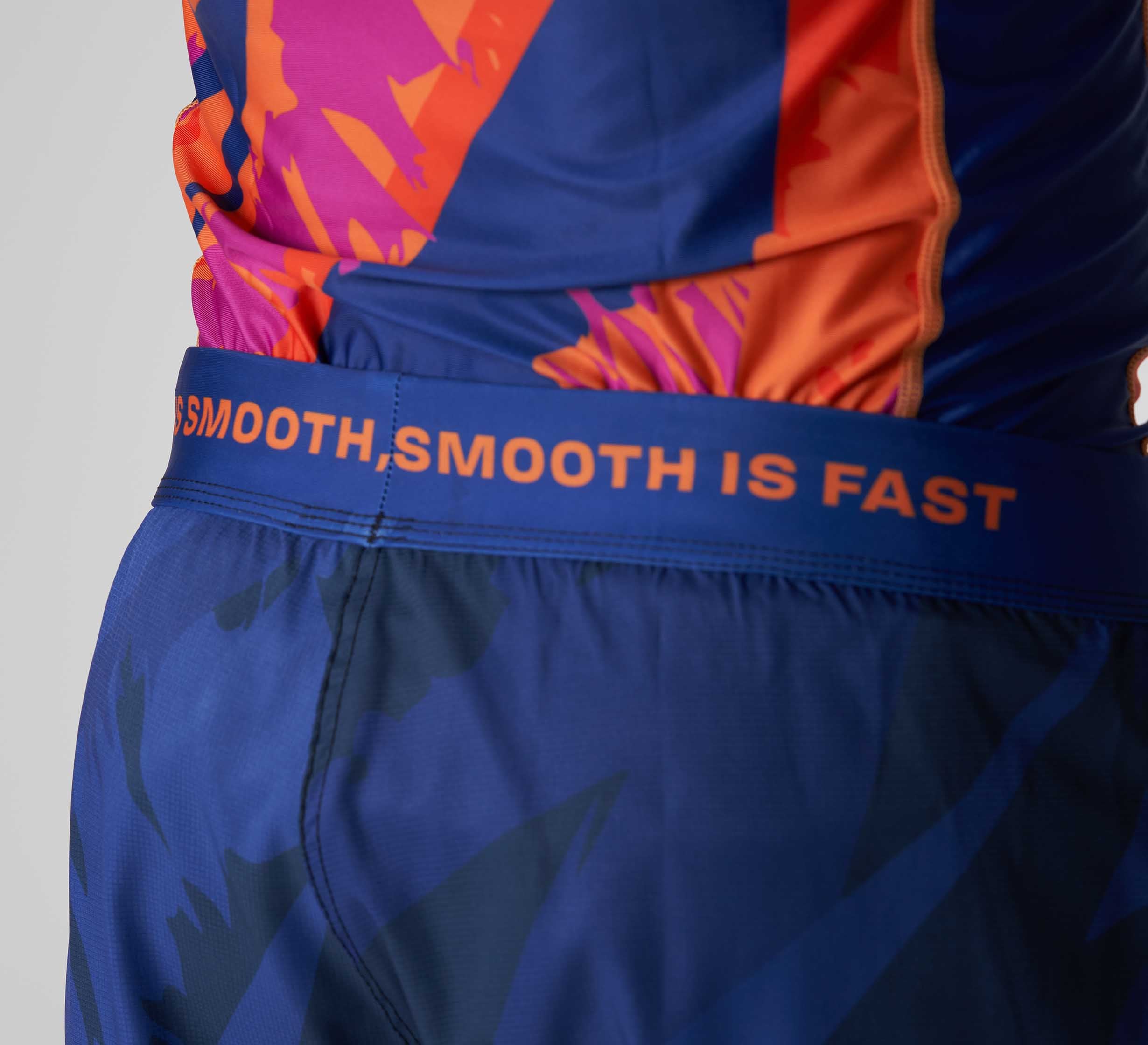 Close-up of a person wearing Hanzo Flex Lite Shorts Blue featuring an orange pattern and “SMOOTH IS FAST” in orange on the waistband. The top has matching abstract orange and pink designs.