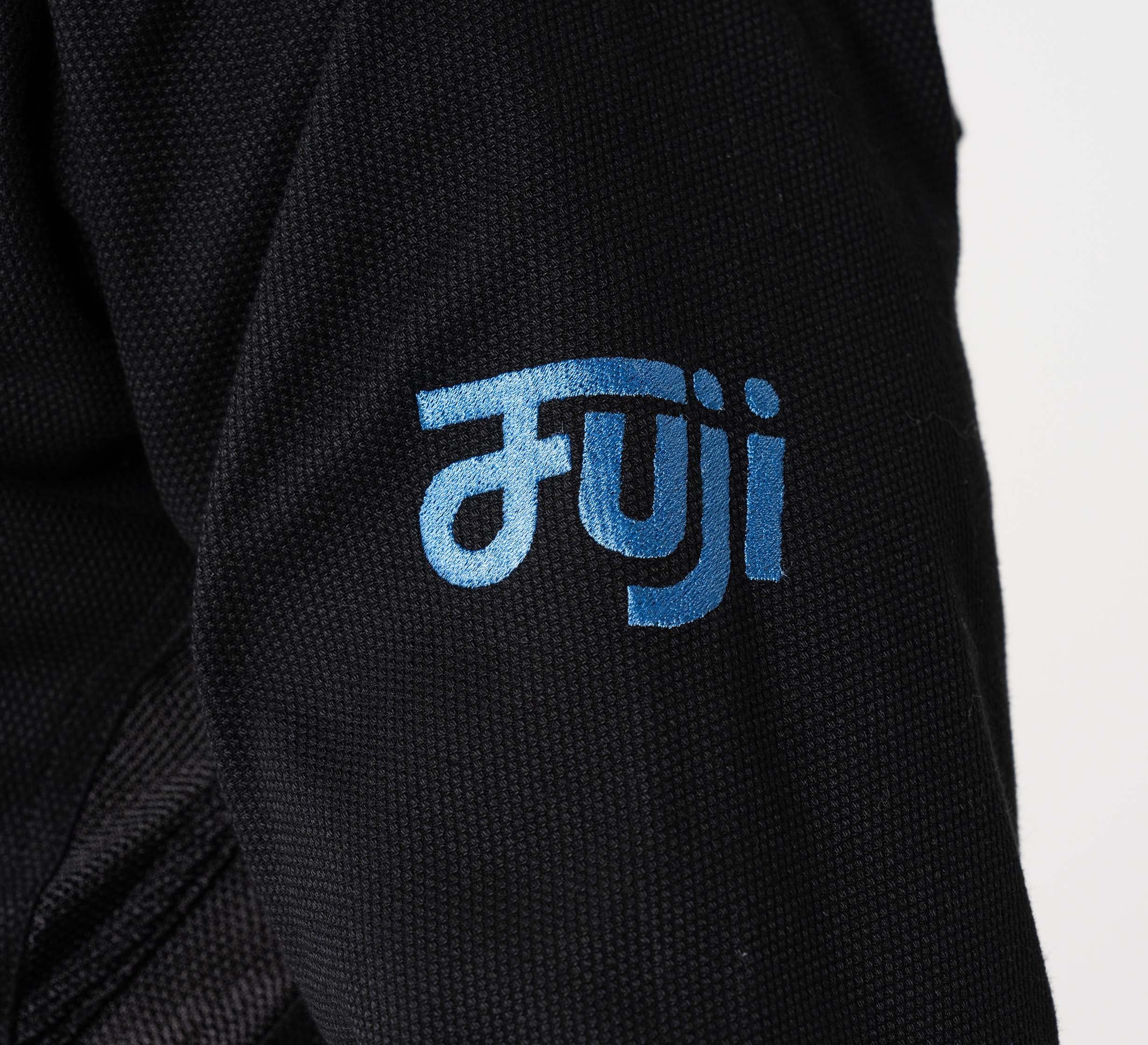 Close-up of the Flow-Tech BJJ Gi in black fabric, featuring "Fuji" embroidered in blue stylized lettering, likely on the uniform or jacket sleeve.
