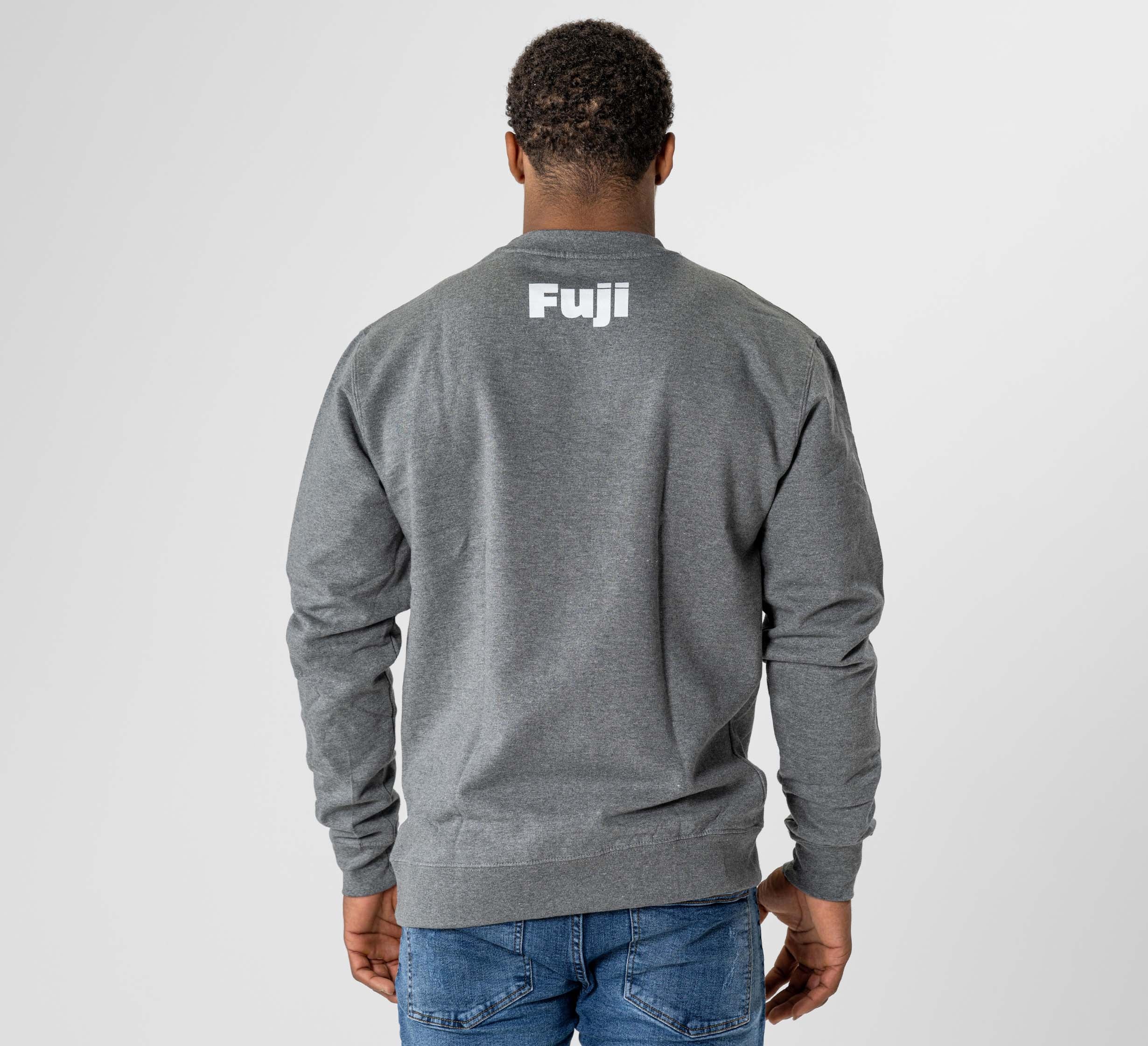 A person stands facing away, hands by their sides, wearing the Jiu Jitsu Player Crewneck Heather Grey with "Fuji" in white on the upper back and blue jeans against a plain light background.
