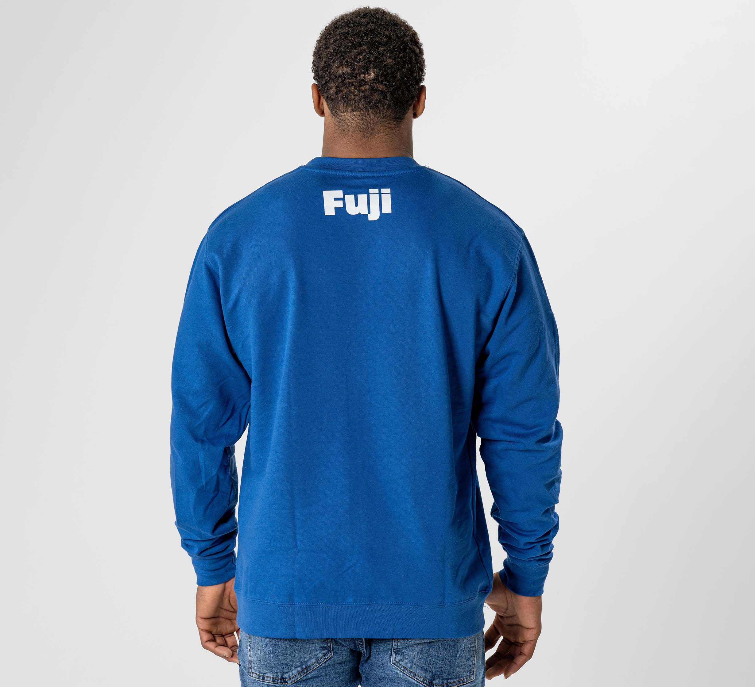 A person stands with their back to the camera against a plain light background, wearing the Jiu Jitsu Player Crewneck Blue sweatshirt featuring "Fuji" printed in white on the back.