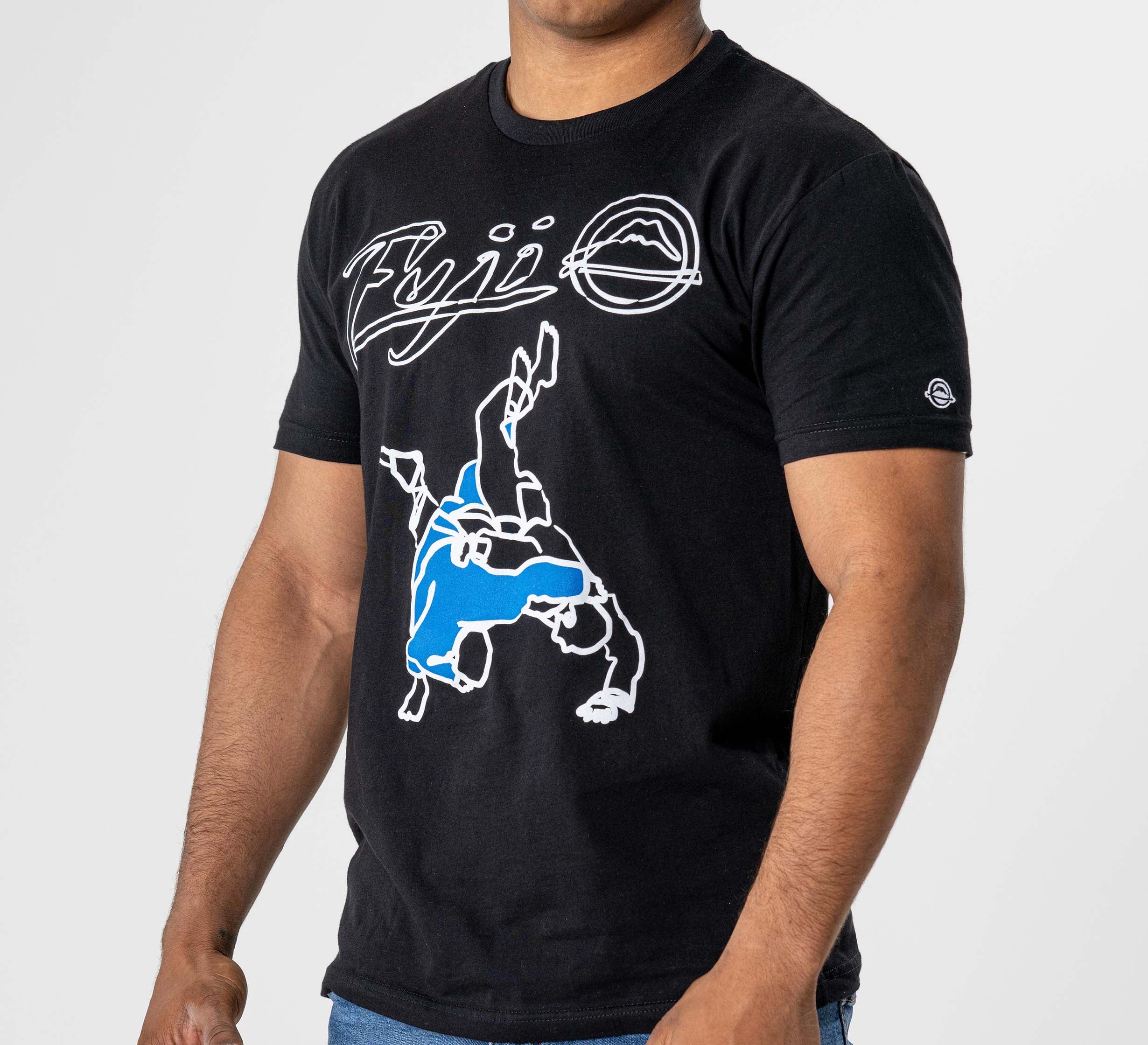 A person wears the FUJI Takedown T-Shirt Black, featuring "Fuji" in white cursive and a graphic of two wrestlers—one in blue—performing a takedown, set against a plain, light background.