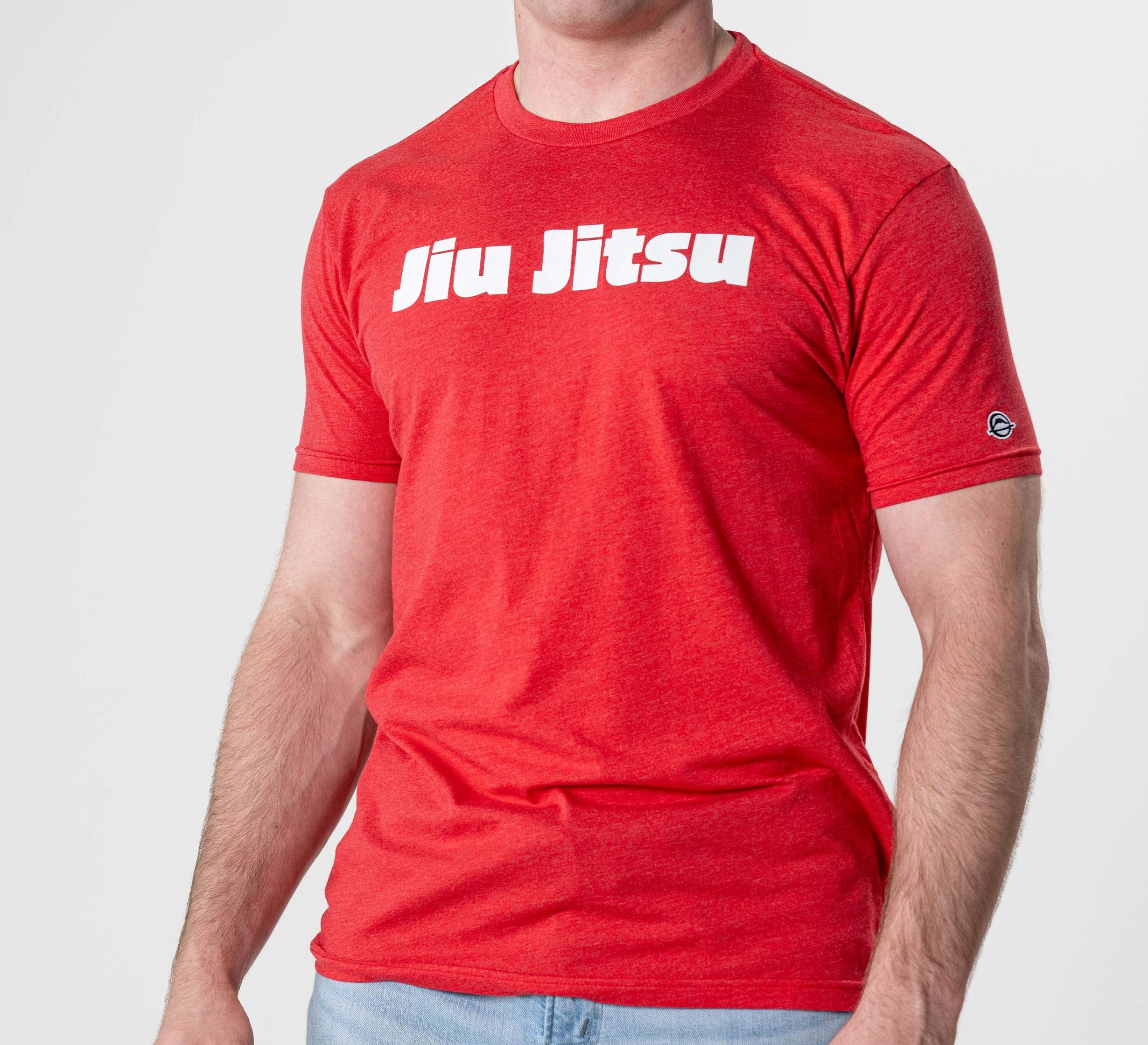 A person wearing the Jiu Jitsu Player T-Shirt Red, featuring bold white "Jiu Jitsu" lettering across the chest, paired with light blue jeans and standing against a plain background.