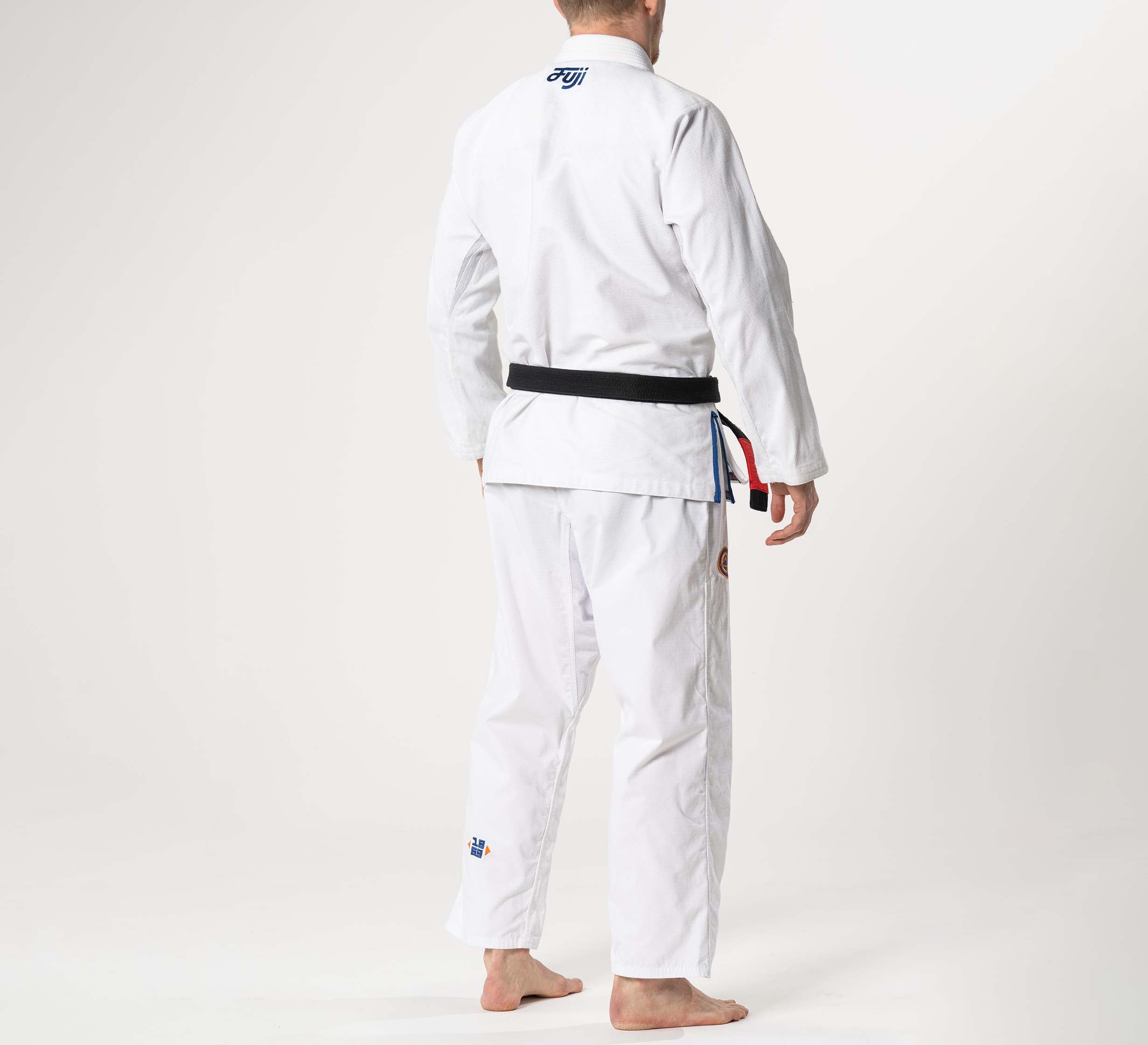 A person is barefoot, seen from behind, wearing the Flow-Tech BJJ Gi in White/Navy/Orange with a black belt against a plain light background.