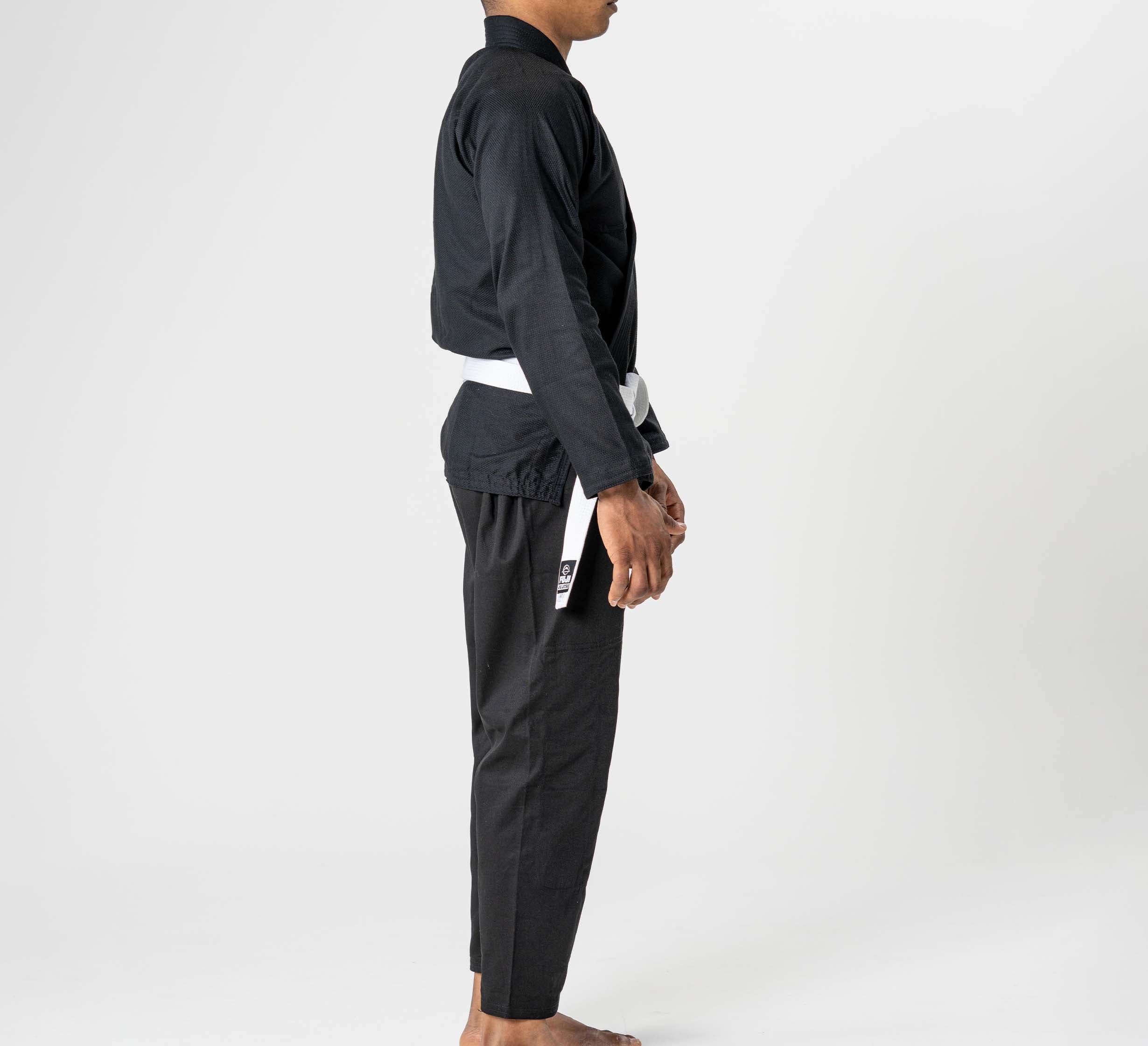 A person wears the Starter Adult BJJ Gi Black with a white belt, standing barefoot in side profile against a plain white background.
