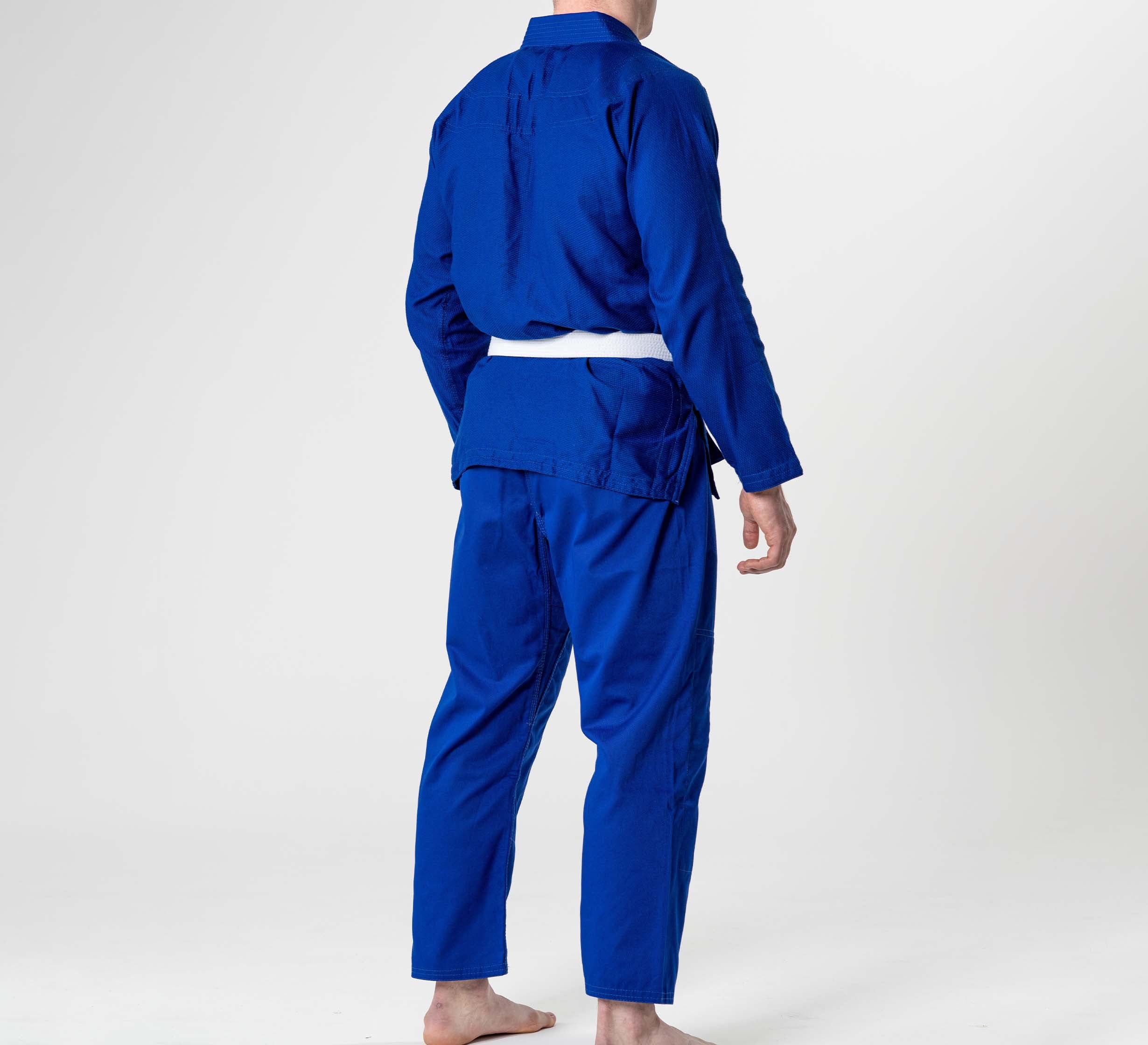 A person stands barefoot on a white background, shown from behind wearing the Starter Adult BJJ Gi Blue with a white belt.