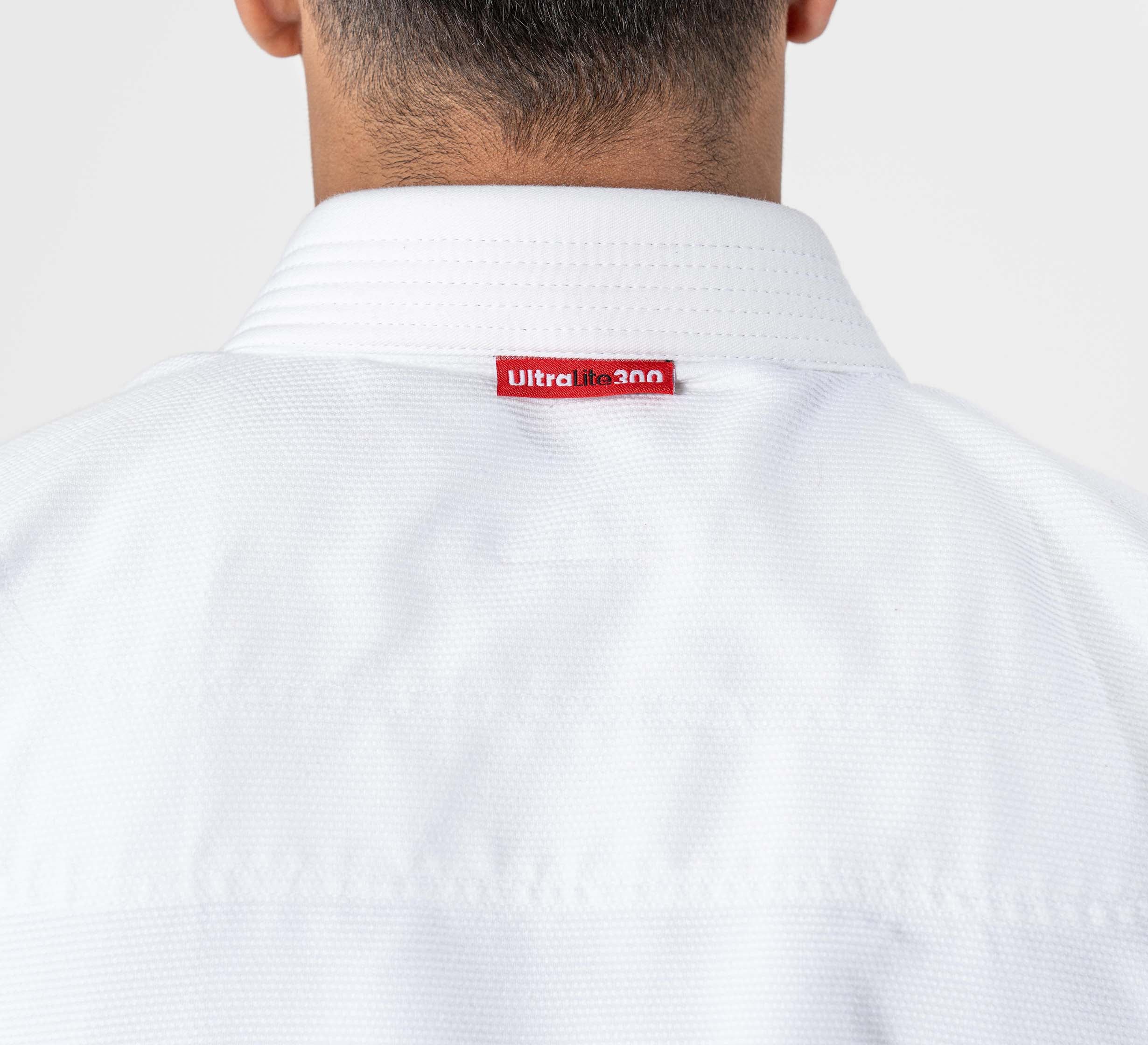 A person wearing the Ultra Lite 300 BJJ Gi White is shown from the back, with a red tag labeled Ultra lite 3.0 on the collar.